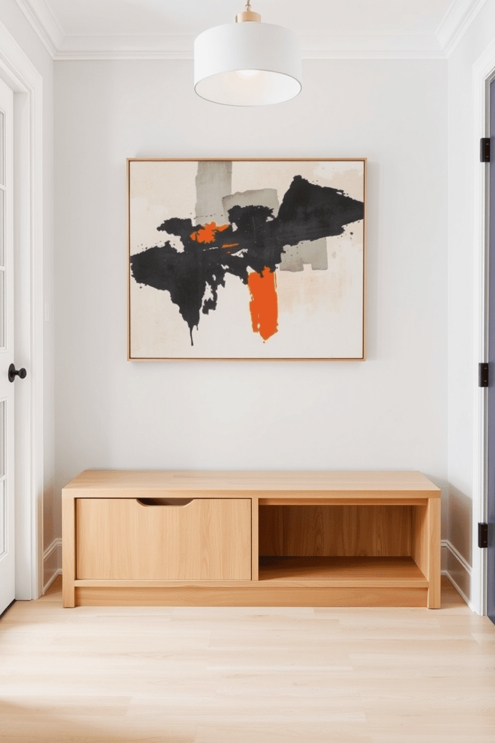 A minimalist bench with hidden storage is positioned against a wall in a bright, airy foyer. The bench features clean lines and a light wood finish, seamlessly blending functionality with elegance. The foyer is adorned with a large, abstract painting above the bench, adding a pop of color to the neutral palette. Soft, ambient lighting from a stylish pendant lamp illuminates the space, creating a welcoming atmosphere.