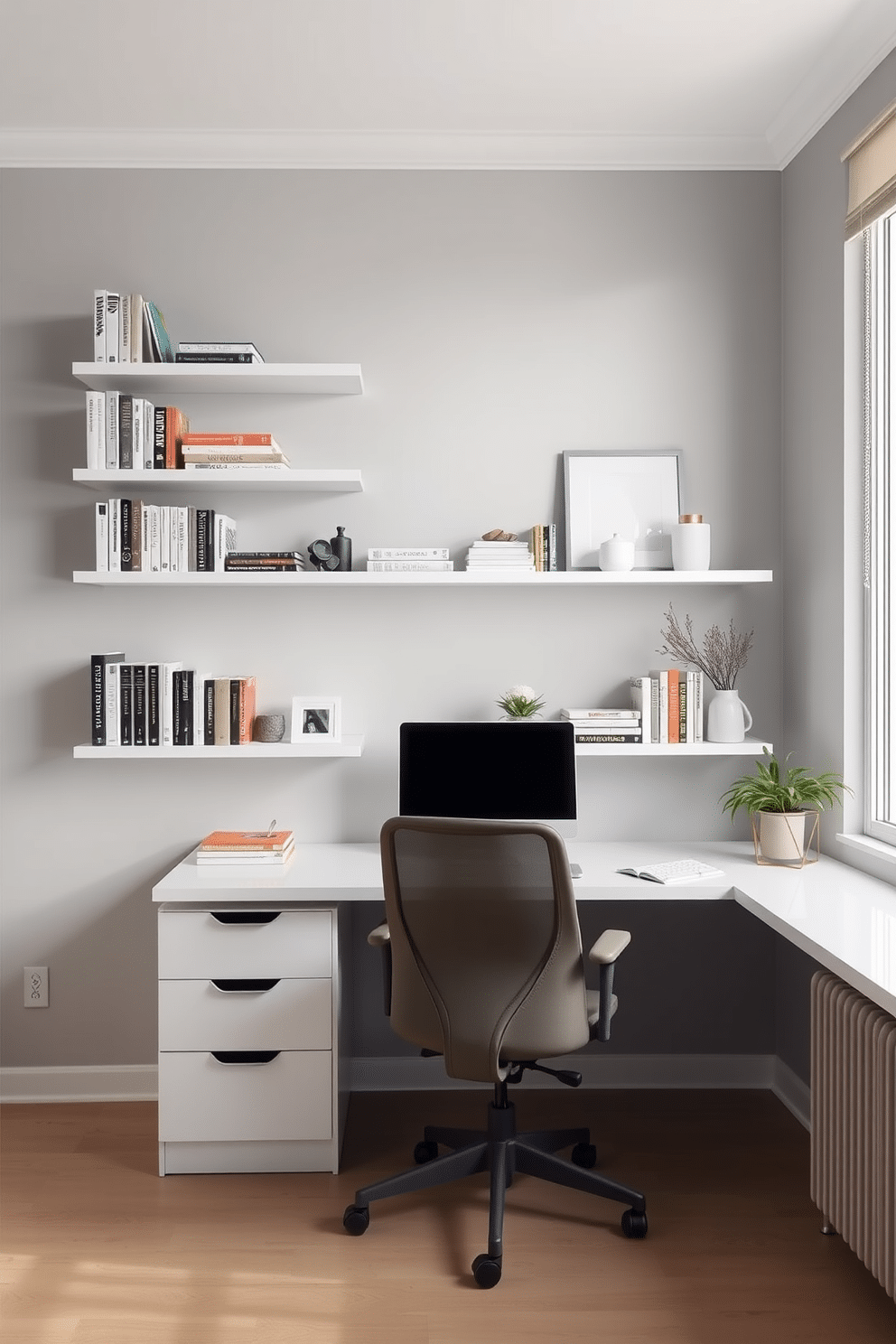 A minimalist desk with a sleek, white surface sits against a soft gray wall. Above the desk, wall-mounted shelves display a curated selection of books and decorative items, creating an organized and airy workspace. The office features a comfortable ergonomic chair in a muted tone, complementing the minimalist aesthetic. Natural light floods the space through a large window, enhancing the serene atmosphere of this modern home office design.