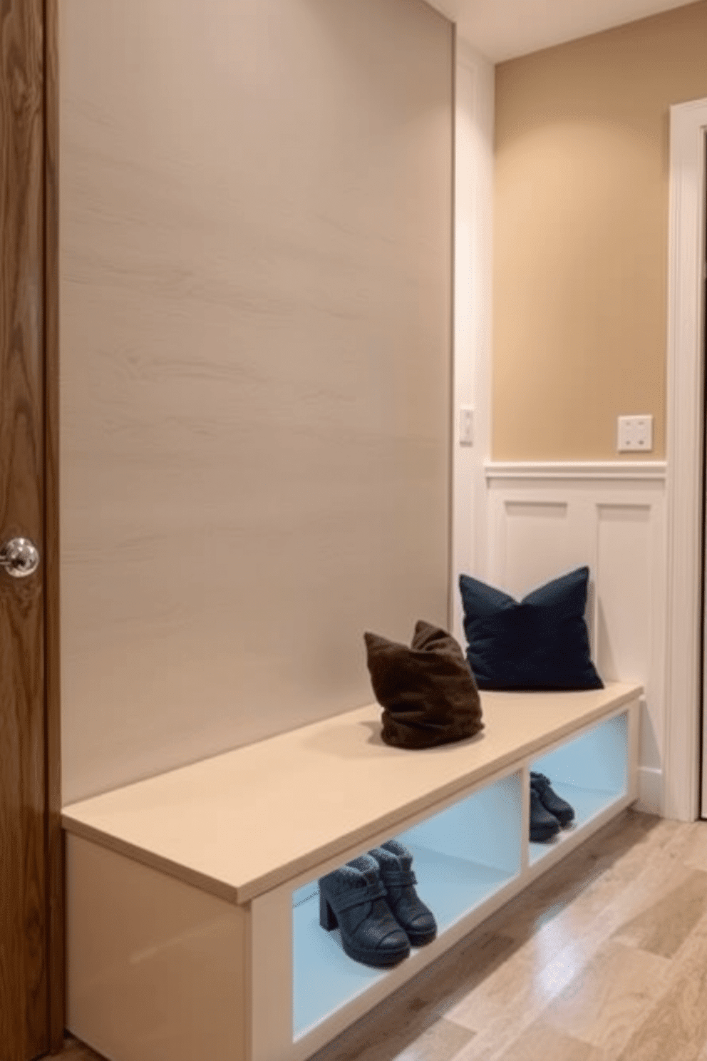 A modern mudroom features a sleek bench with built-in storage underneath, illuminated by stylish accent lighting that highlights its clean lines. The walls are adorned with a combination of textured wood paneling and soft, neutral paint, creating a warm and inviting atmosphere.