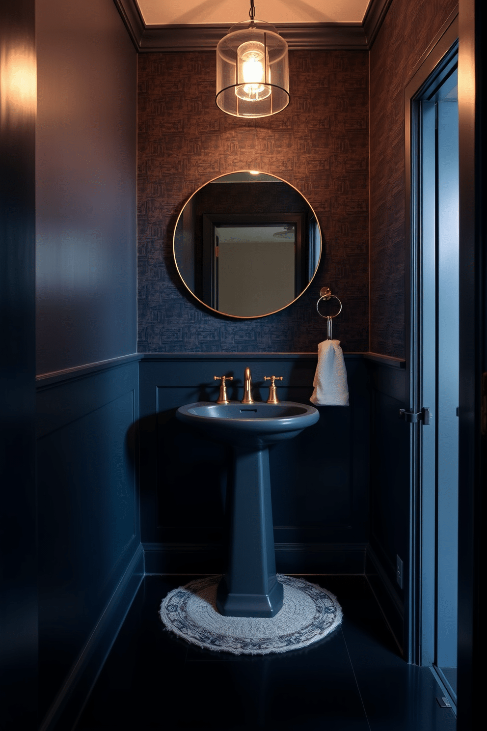 A stylish pedestal sink in dark tones stands elegantly against a backdrop of deep navy walls, creating a dramatic focal point. The sink is complemented by sleek gold fixtures and a minimalist round mirror that reflects the ambient light, enhancing the moody atmosphere of the powder room. Rich, textured wallpaper adds depth to the space, while a small, geometric-patterned rug anchors the room, providing contrast against the dark flooring. Soft, ambient lighting from a chic pendant fixture casts a warm glow, inviting a sense of intimacy and sophistication.