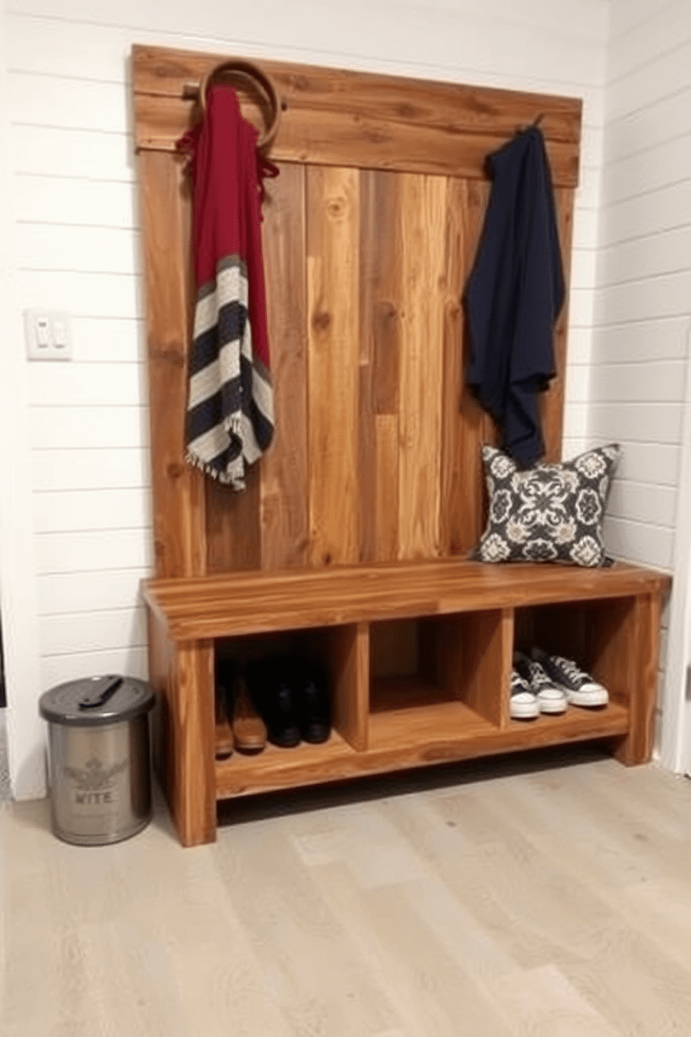 A rustic mudroom bench made from reclaimed wood features multiple storage cubbies underneath for shoes and outdoor gear. The bench is complemented by a backdrop of shiplap walls painted in a soft white, creating a bright and welcoming entryway.