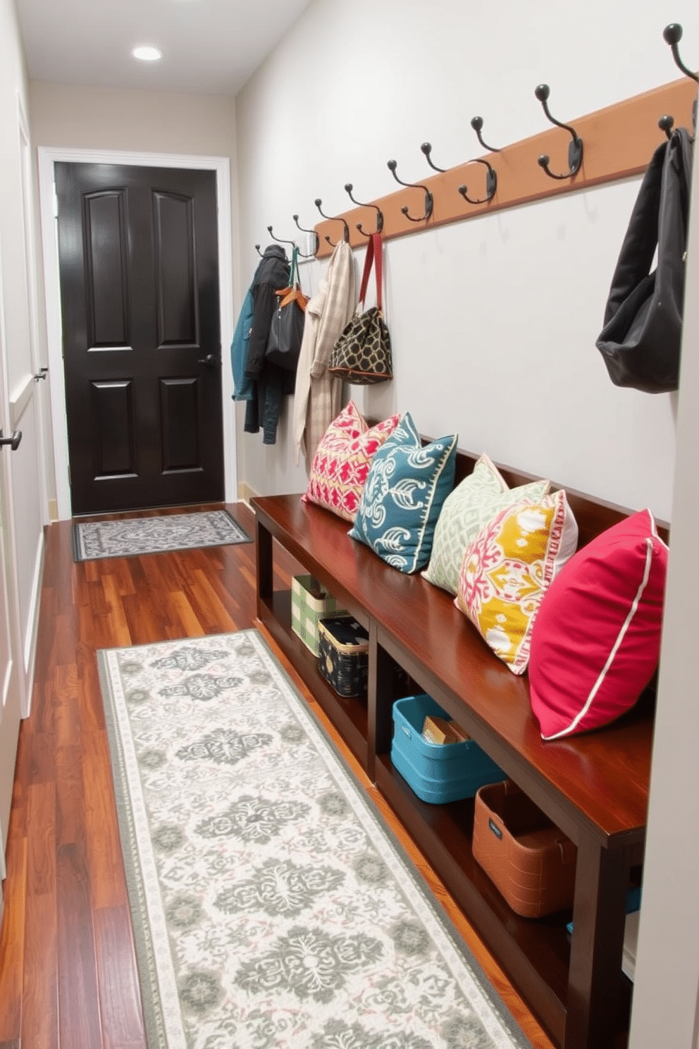 A stylish mudroom features a long wooden bench adorned with colorful decorative pillows that add a pop of color and comfort. The bench is positioned against a wall with hooks above for hanging coats and bags, while a patterned rug lies beneath, enhancing the cozy atmosphere.