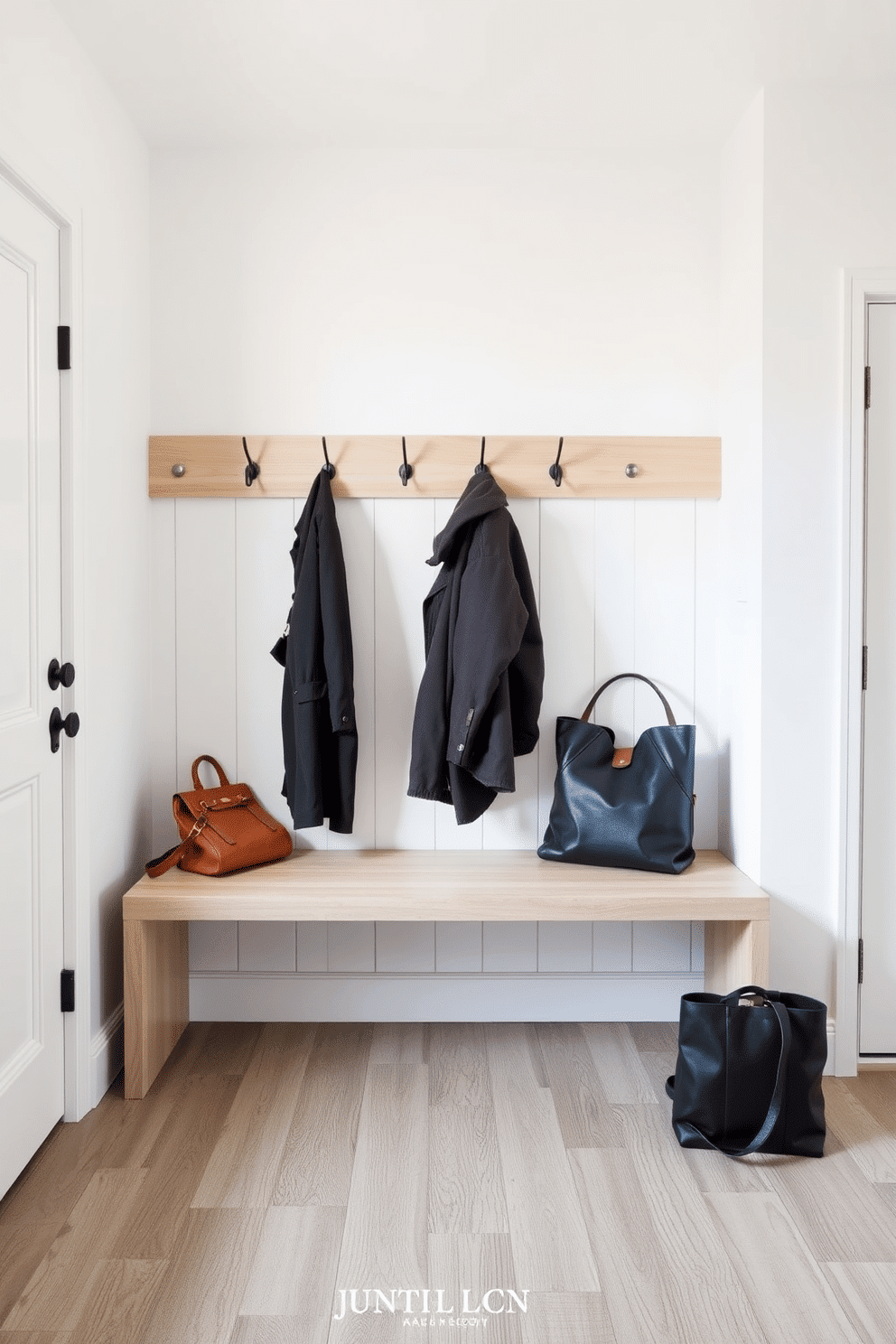 A modern minimalist bench with sleek lines sits against a wall in a bright, airy mudroom. The bench features a smooth, light wood finish and is complemented by a series of neatly arranged hooks above for coats and bags.