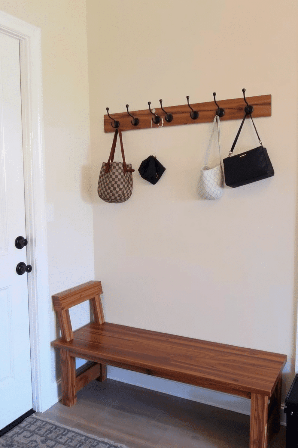 A simple bench with a rustic finish sits against the wall, crafted from reclaimed wood that showcases its natural grain and imperfections. Above the bench, a series of hooks are mounted for hanging coats and bags, creating an inviting and functional mudroom space.