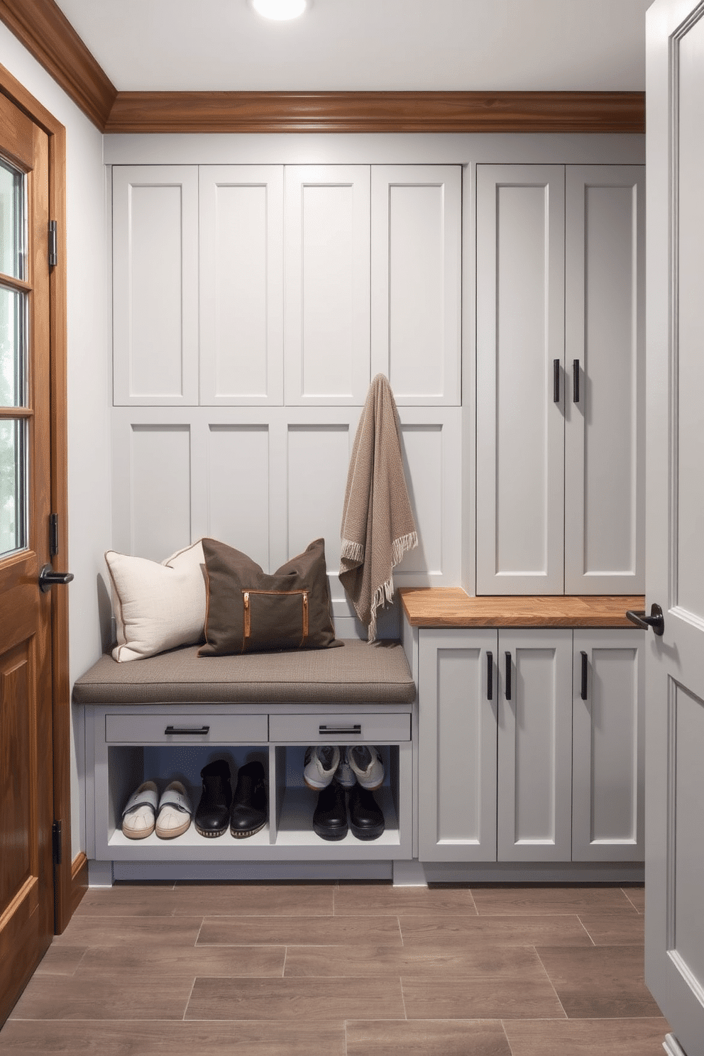 A stylish mudroom features a built-in bench with shoe storage drawers underneath, providing both functionality and aesthetic appeal. The bench is upholstered in a durable fabric, while the cabinetry is painted in a soft gray, complementing the warm wood accents throughout the space.