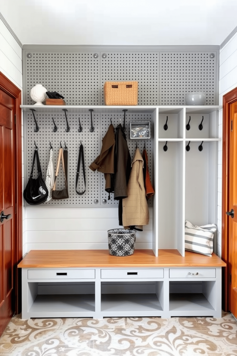 A pegboard wall is designed with a grid layout, featuring various hooks and shelves for versatile hanging options. It is painted in a soft gray color, creating a modern and functional space that enhances organization. The mudroom closet is equipped with built-in cubbies and a bench for seating, finished in a warm wood tone. The walls are adorned with shiplap, and the floor is laid with durable, patterned tile to withstand high traffic.