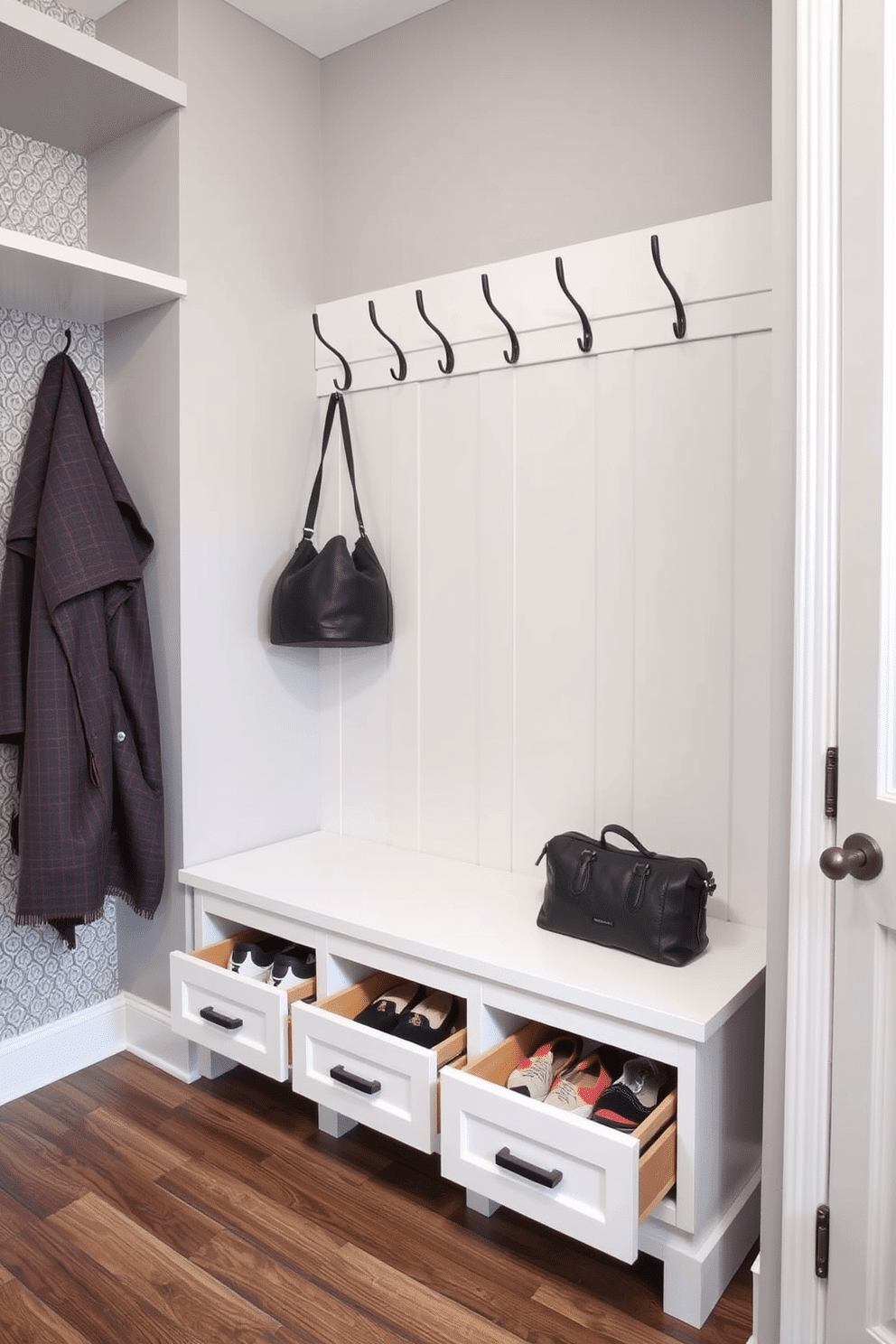 A functional mudroom closet features a stylish bench with pull-out drawers for hidden storage, providing a clean and organized space for shoes and outdoor gear. The walls are painted in a soft gray, complemented by a patterned wallpaper on one side, while hooks for coats and bags are neatly arranged above the bench.