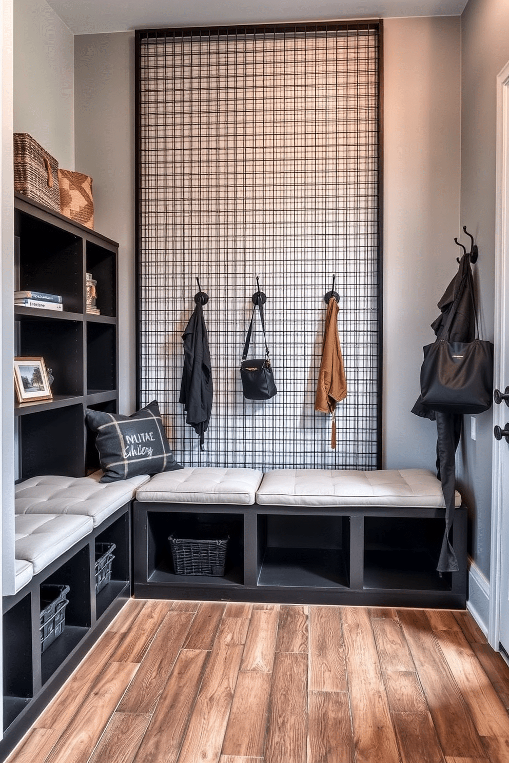 A striking mudroom featuring a metal grid wall that adds an industrial flair. The space includes a built-in bench with plush seating, surrounded by open shelving for storage and decorative accents. The floor is adorned with rustic wood planks, while the walls are painted in a soft gray to enhance the industrial vibe. Hooks for coats and bags are mounted on the metal grid, creating a functional yet stylish entryway.