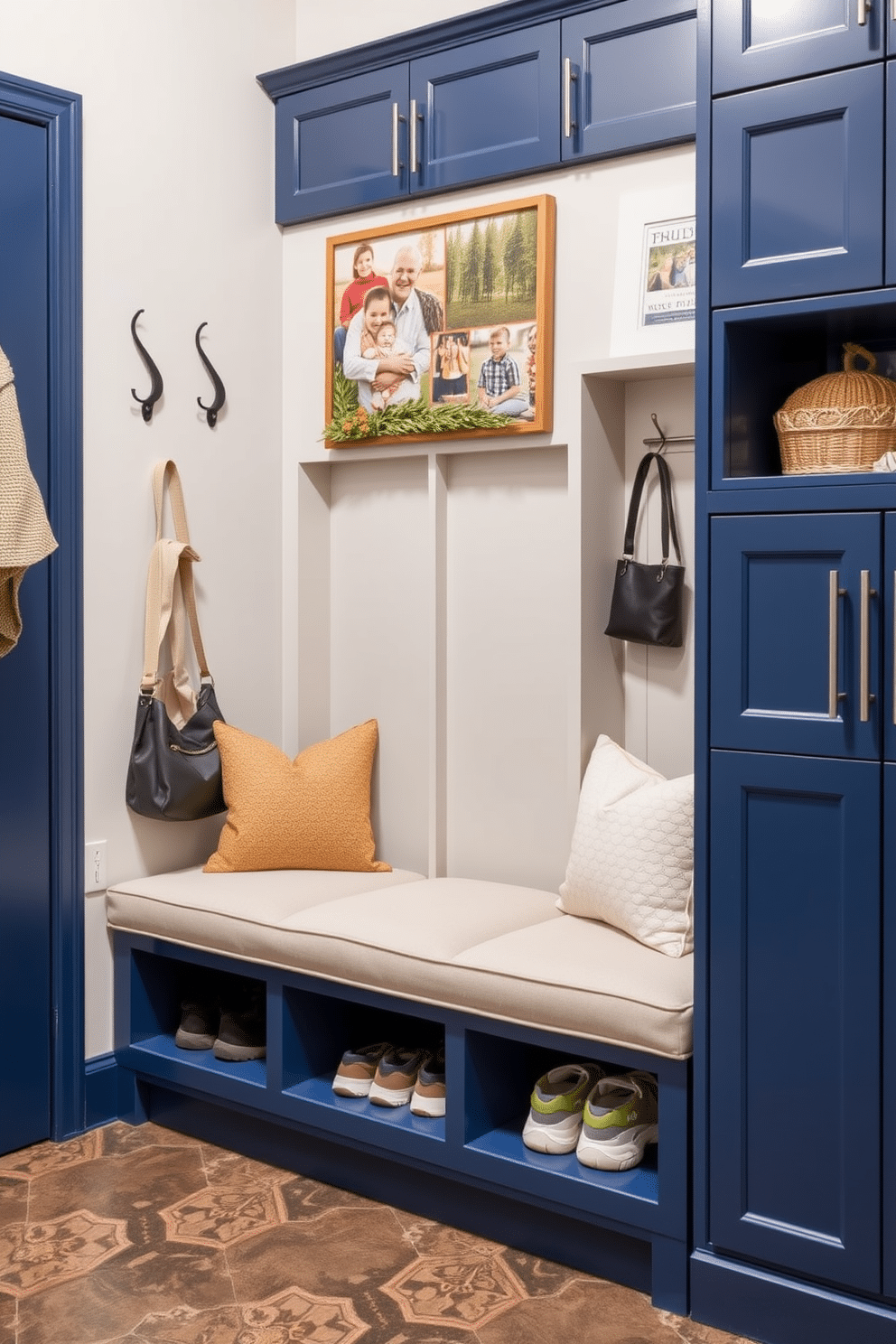 A navy blue mudroom bench features a sleek, modern design with plush cushions and integrated storage underneath. The walls are adorned with hooks for coats and bags, while the floor is covered with a durable, patterned tile that adds a touch of style. The cubby design incorporates open shelving for easy access to shoes and accessories, framed by navy blue cabinetry that complements the bench. Above the cubbies, a decorative board displays family photos and seasonal decor, creating a welcoming and organized space.