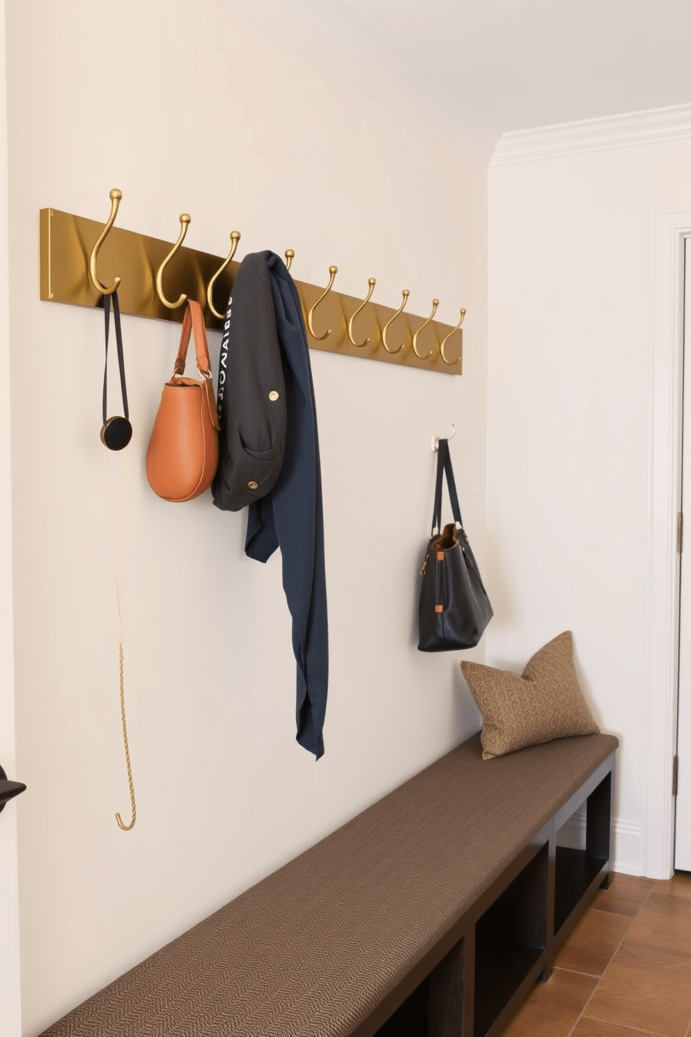 A welcoming mudroom features a row of stylish wall hooks made of brushed brass, perfect for hanging coats and bags. The space is designed with a durable, textured bench for sitting while removing shoes, and the walls are painted a soft, neutral color to create a warm atmosphere.