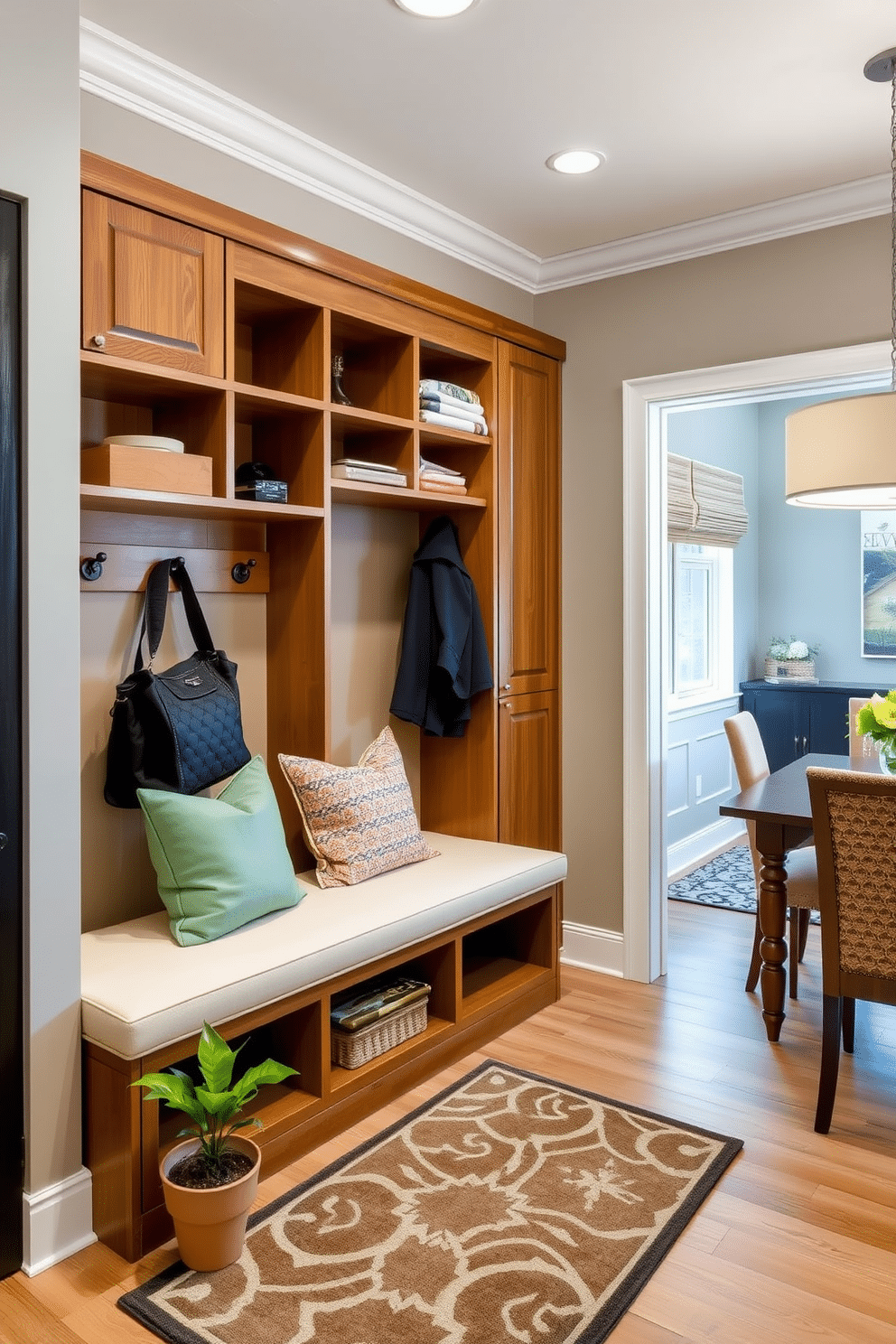 A stylish mudroom adjacent to a dining room features vertical storage solutions that maximize space efficiency. The design includes built-in shelves and hooks for coats and bags, with a sleek bench for seating and a pop of color from decorative cushions. The mudroom's walls are painted in a soft gray, complementing the warm wood tones of the cabinetry. A patterned rug adds texture to the floor, while a small potted plant brings a touch of greenery to the space.