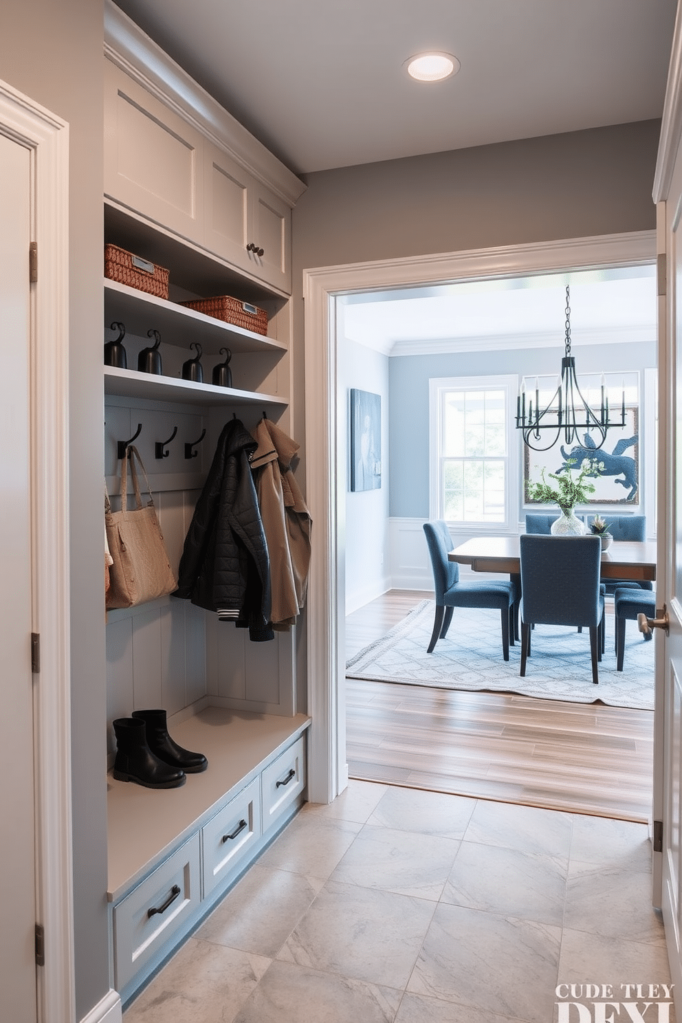 A stylish mudroom adjacent to the dining room features built-in hooks and open shelves for easy organization. The walls are painted a soft gray, and the flooring consists of durable, weather-resistant tiles in a neutral tone.