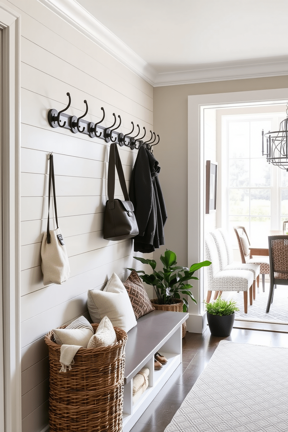 A stylish mudroom features a row of elegant hooks mounted on a shiplap wall, perfect for hanging coats and bags. Beneath the hooks, a bench with plush cushions provides a comfortable spot to sit while putting on shoes, and a woven basket adds texture and storage. Adjacent to the dining room, the mudroom blends seamlessly with the decor, showcasing a color palette that complements the dining area. Large windows allow natural light to flood in, illuminating the space and highlighting decorative elements like framed artwork and potted plants.