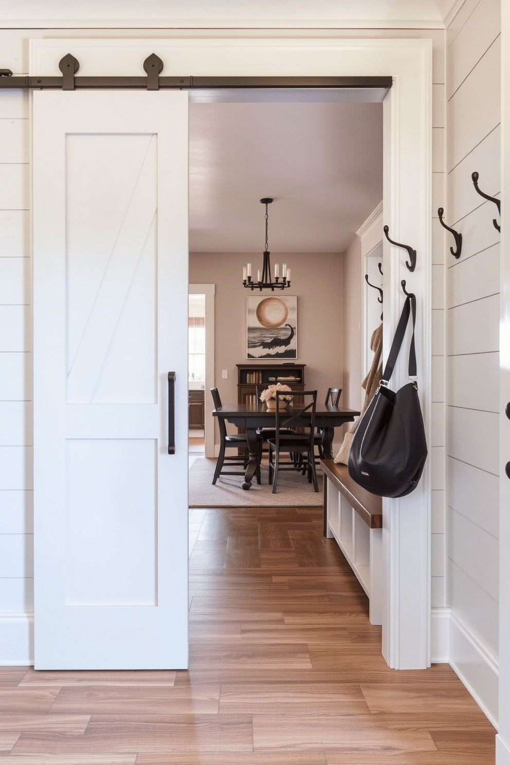 A stylish mudroom featuring a sliding barn door that opens to a spacious area with rustic charm. The walls are adorned with shiplap, and a built-in bench with storage cubbies provides a functional yet inviting space for shoes and outerwear. Adjacent to the dining room, this mudroom design seamlessly blends practicality with aesthetics. The flooring is a durable tile that mimics wood, and decorative hooks line the wall, perfect for hanging coats and bags.