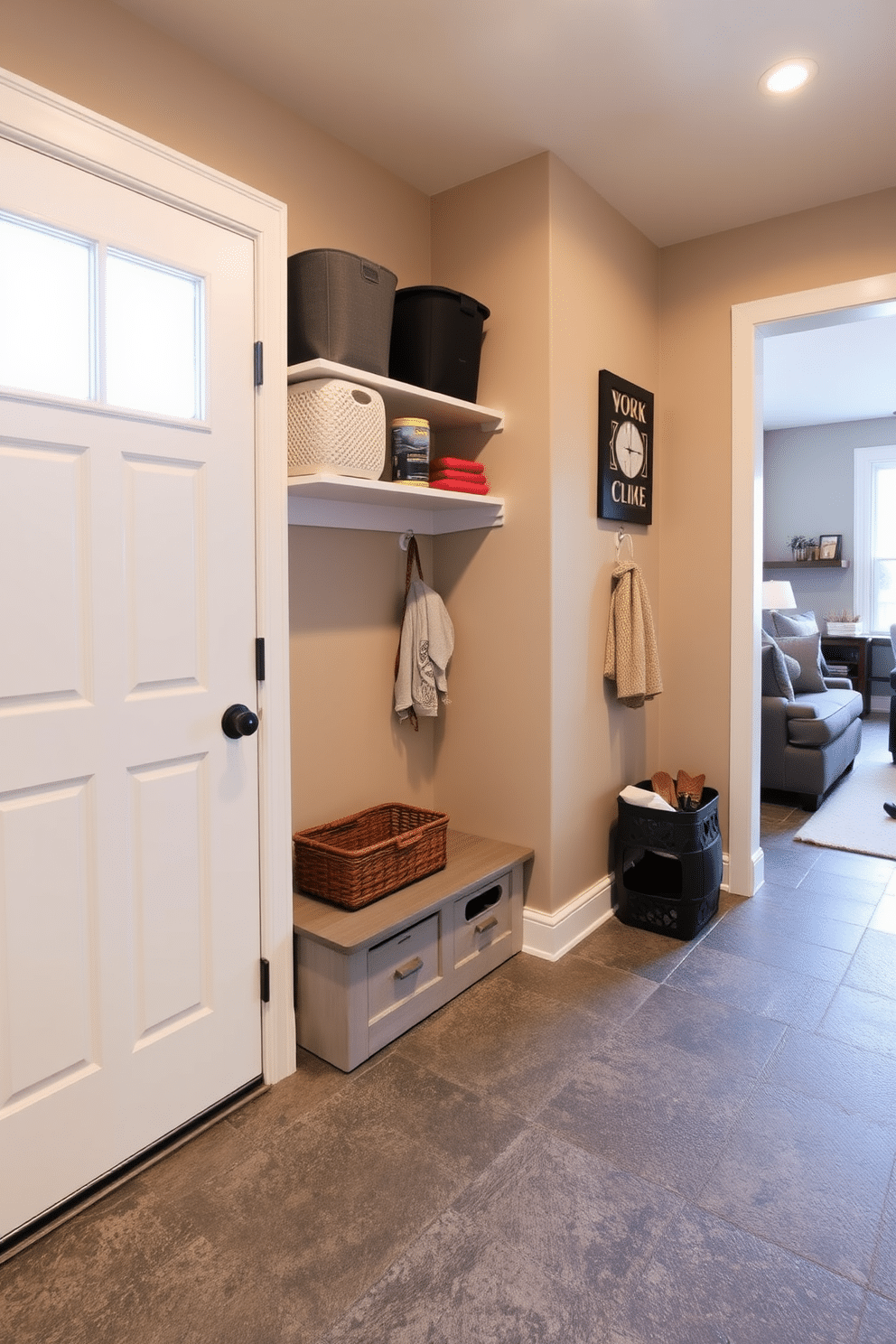 A functional mudroom near the family room features open shelving for easy access to everyday items, allowing for a clutter-free entryway. The walls are painted in a warm beige tone, complemented by a durable, textured floor in a dark gray hue, creating a welcoming space for family and guests.