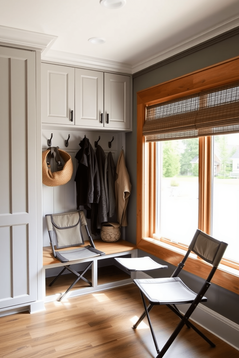 A stylish mudroom adjacent to the garage features compact folding chairs that can be easily stowed away when not in use. The space is designed with a functional bench, hooks for coats, and a combination of light gray cabinetry and warm wood accents to create an inviting atmosphere. The folding chairs are upholstered in a durable, weather-resistant fabric, perfect for quick seating as you enter the home. Natural light floods the room through a large window, highlighting the organized storage solutions and decorative elements that enhance the overall design.