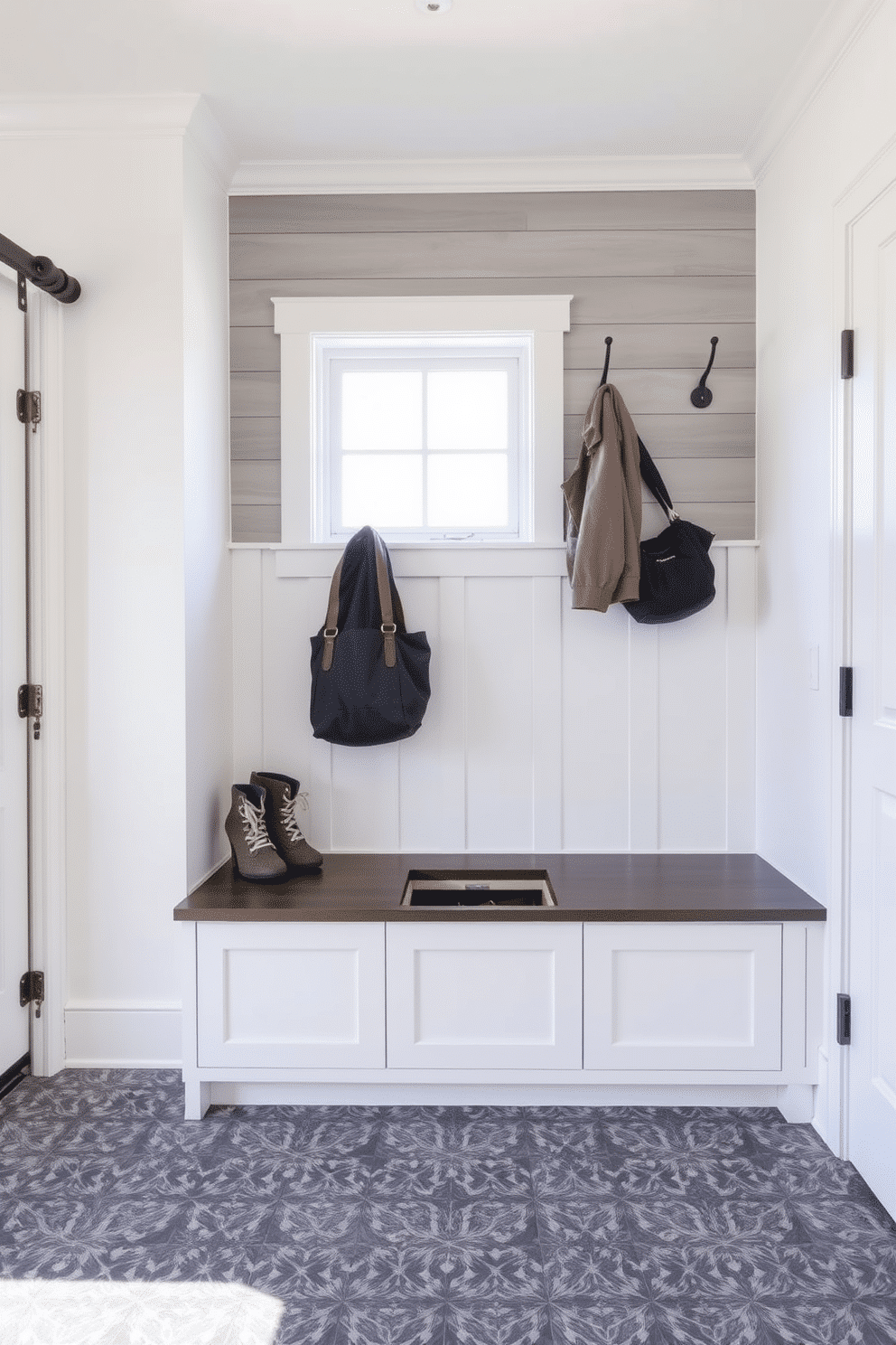 A functional mudroom near the garage features a sleek bench with a lift-top storage compartment, ideal for stowing away shoes and outdoor gear. The walls are painted a crisp white, complemented by a textured gray shiplap accent wall, creating a bright and inviting space. Above the bench, a series of hooks are mounted for coats and bags, while a large window allows natural light to flood the area. The floor is adorned with durable, patterned tiles that are easy to clean, enhancing the practicality of this stylish mudroom design.