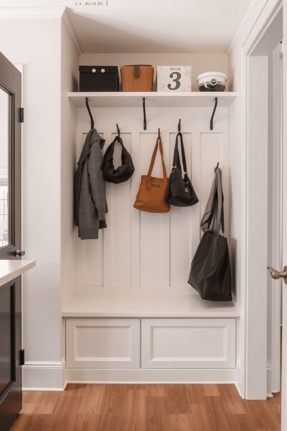 A functional drop zone for keys and bags, seamlessly integrated into the mudroom near the kitchen. The space features a built-in bench with storage underneath, surrounded by hooks for coats and bags, all accented by a soft, neutral color palette.