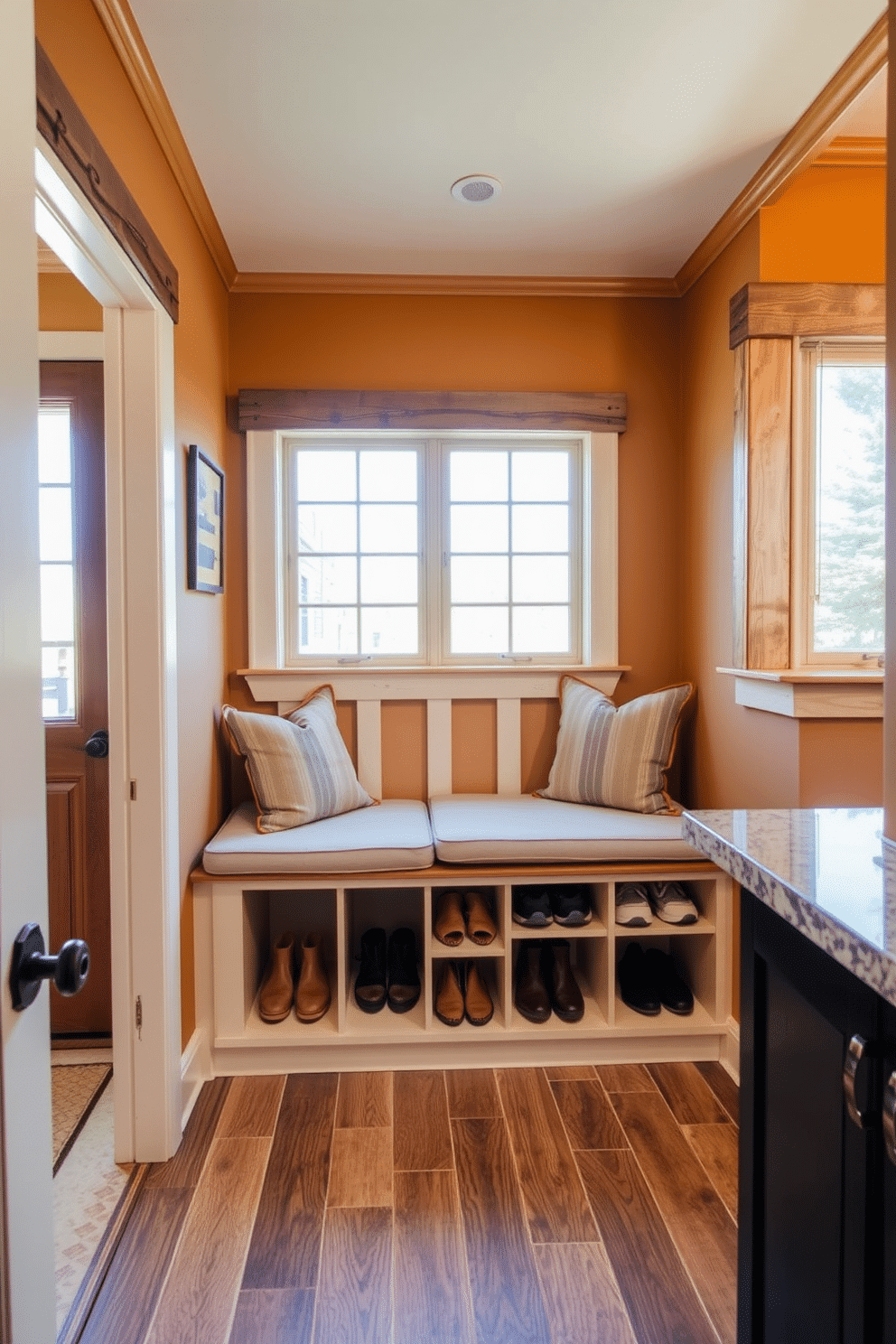 A cozy mudroom features a built-in bench with soft cushions, providing a comfortable spot to sit while putting on shoes. Below the bench, spacious cubbies are designed to neatly store shoes and outdoor gear, keeping the area organized and clutter-free. The walls are painted in a warm, inviting color, complemented by rustic wood accents that add charm to the space. Natural light floods in through a nearby window, enhancing the welcoming atmosphere of this functional mudroom near the kitchen.