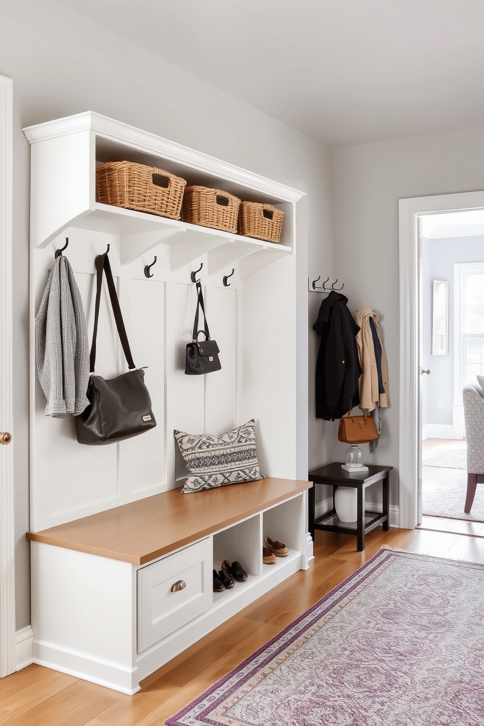 A stylish mudroom seamlessly integrates with the living room, featuring multi-functional furniture that enhances versatility. A built-in bench with storage below provides seating and space for shoes, while overhead shelves display decorative baskets for organization. The walls are painted in a soft gray, creating a calm atmosphere, and a durable, patterned rug adds texture to the floor. A combination of hooks and a hanging rack keeps coats and bags easily accessible, while a small side table offers a spot for keys and mail.