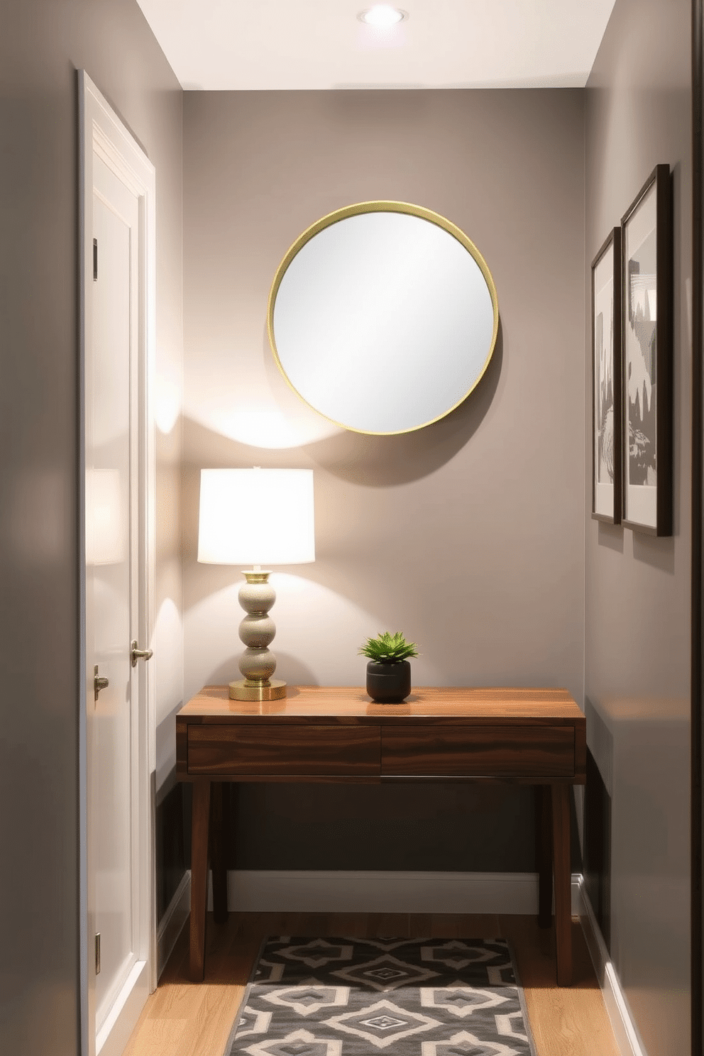 A narrow entryway featuring a sleek console table with a rich walnut finish, adorned with a stylish lamp that casts warm accent lighting. The walls are painted in a soft gray, complemented by a geometric patterned runner that adds a touch of elegance to the space. On the opposite wall, a series of framed artwork adds personality, while a small potted plant on the table brings in a hint of greenery. Above the console, a round mirror with a brushed gold frame reflects light, creating an inviting atmosphere.