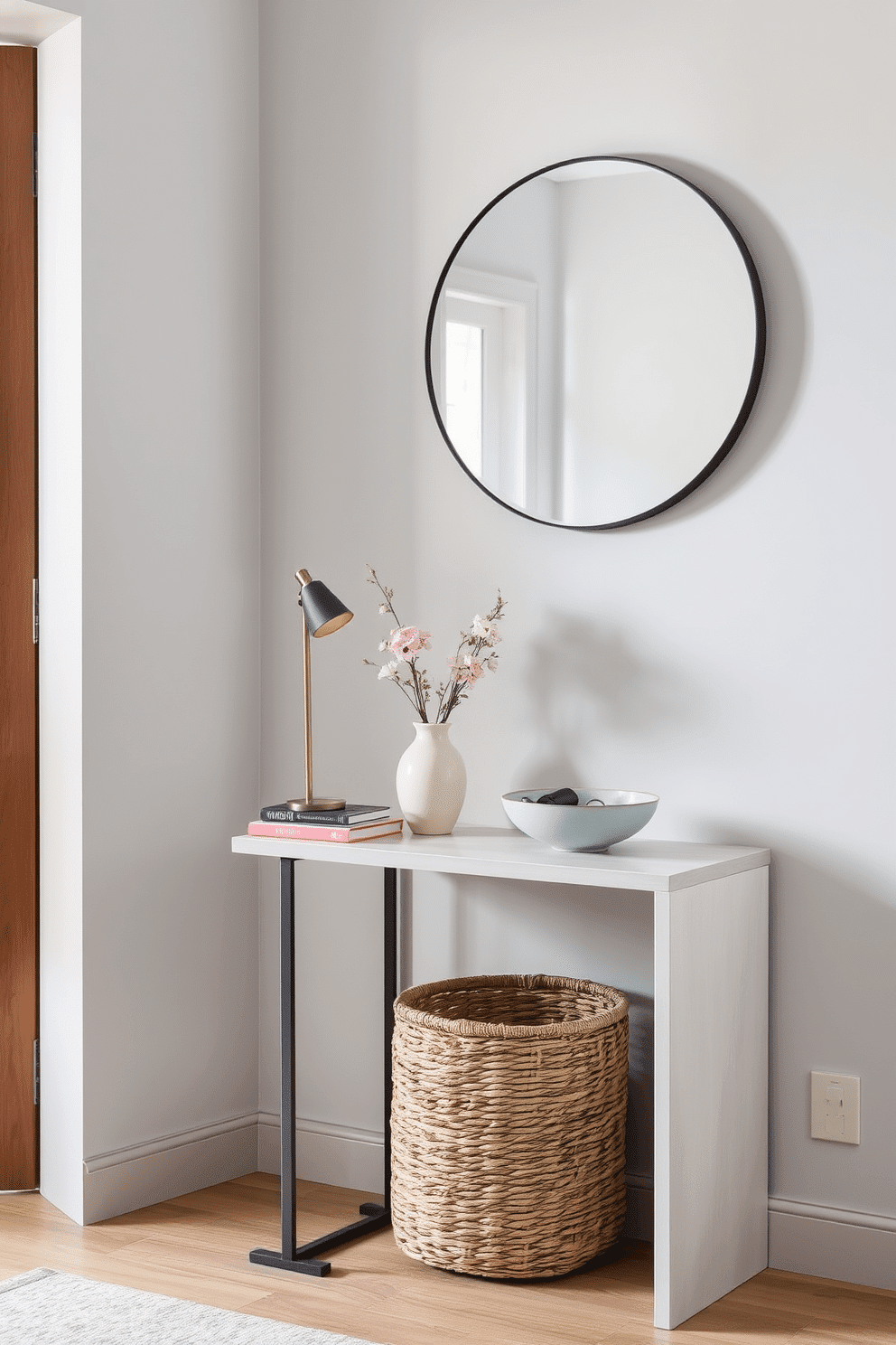 A narrow side table is positioned against a light gray wall, adorned with a sleek lamp and a small stack of art books. A delicate ceramic vase with fresh flowers adds a touch of color, while a stylish bowl holds keys and small trinkets. The entryway features a minimalist design with a narrow console table and a large round mirror above it. Soft lighting highlights the space, while a woven basket underneath provides convenient storage for shoes and accessories.