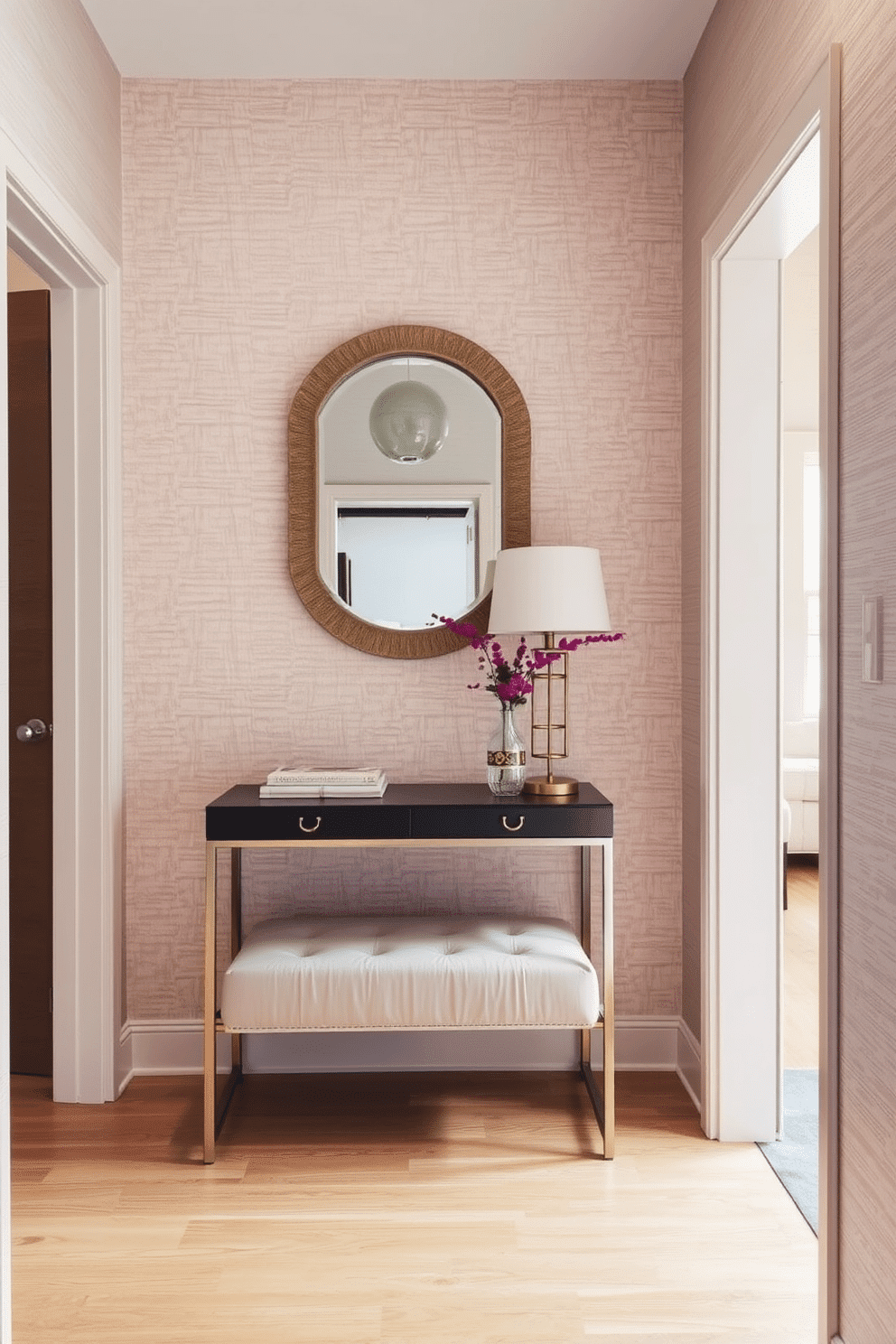 A narrow entryway features textured wallpaper that adds depth and character to the space. The flooring is a warm wood, and a sleek console table with a decorative mirror above it enhances the inviting atmosphere. The wallpaper showcases a subtle pattern in soft hues, creating a cozy yet elegant backdrop. A small bench with storage underneath provides functionality while maintaining a stylish look.