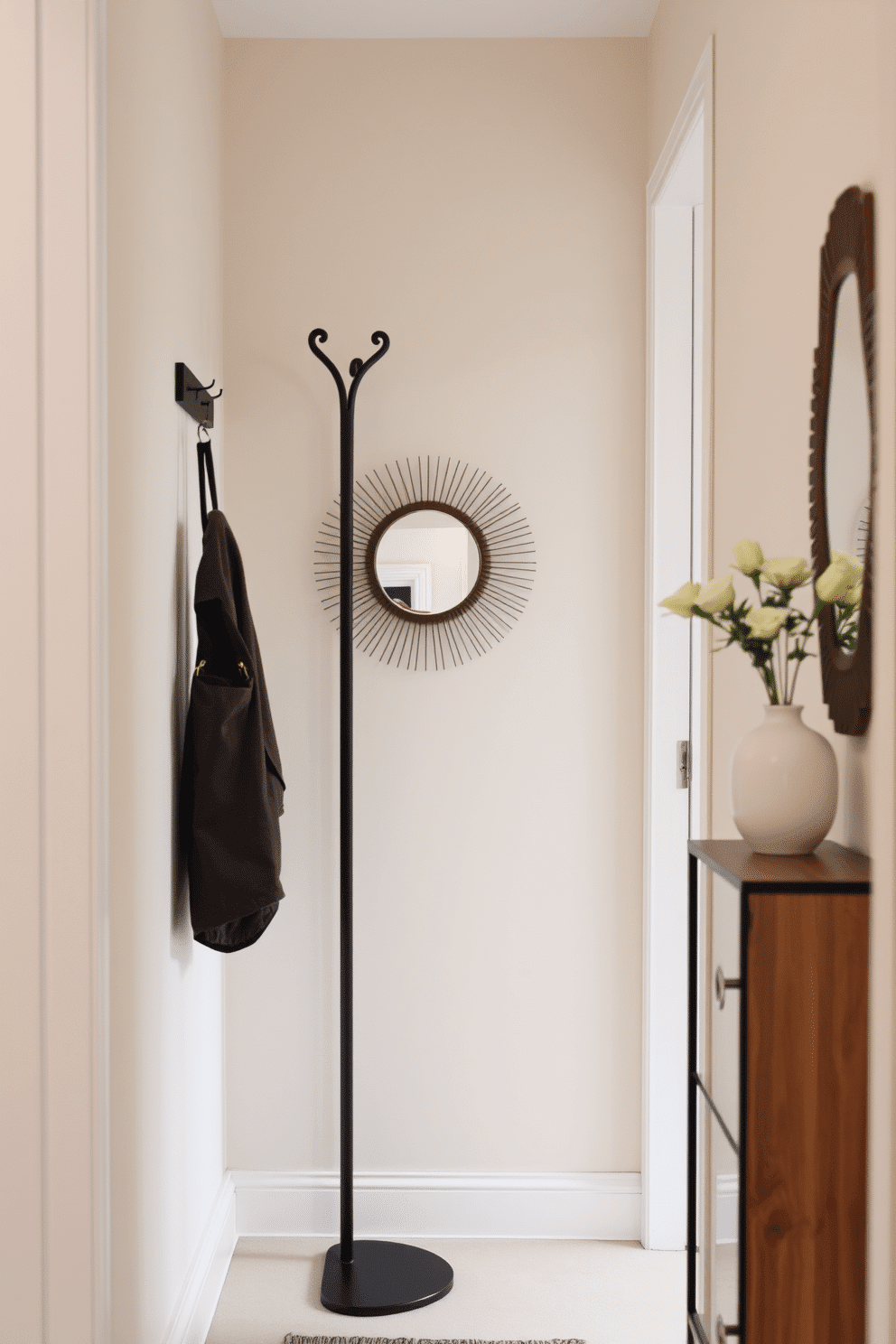 A vertical coat rack stands elegantly in a narrow entryway, crafted from sleek metal with a matte black finish. Its minimalist design complements the surrounding decor while providing ample space for hanging coats and accessories. The walls are painted in a soft, neutral tone, enhancing the sense of openness in the compact area. A small console table with a decorative mirror above it adds functionality and style, creating an inviting atmosphere for guests.