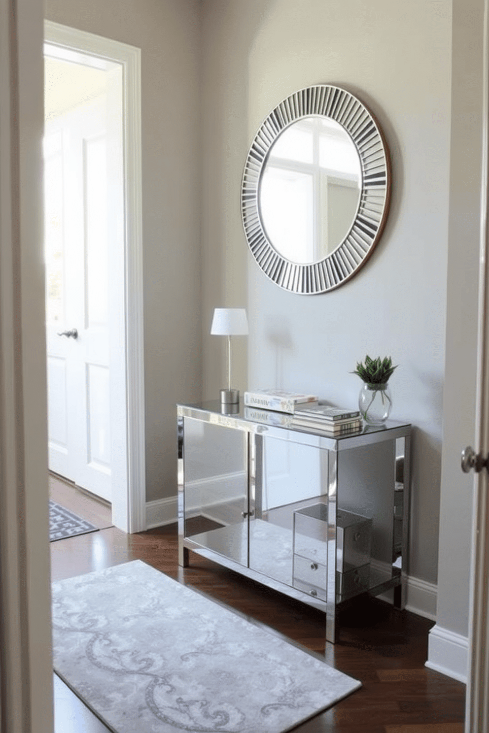 A narrow foyer features mirrored furniture that enhances the sense of space and reflects natural light throughout the area. A sleek console table with a mirrored surface is paired with a decorative round mirror above it, creating a stunning focal point. The walls are painted in a soft, neutral tone to complement the reflective surfaces, while a stylish runner rug adds warmth and texture underfoot. Potted plants on either side of the console bring a touch of greenery, further brightening the entrance.