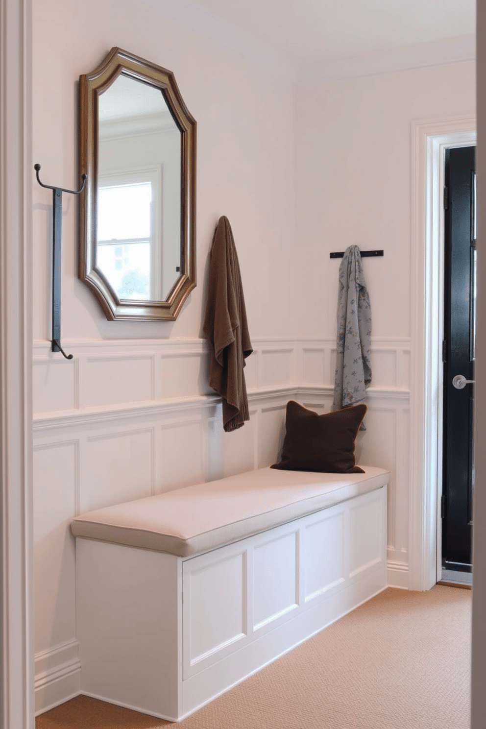 A narrow foyer features a built-in bench with hidden storage underneath, allowing for a tidy and functional entryway. The bench is upholstered in a soft, neutral fabric, complemented by a sleek, modern coat rack mounted on the wall. The walls are adorned with light-colored wainscoting, creating an inviting atmosphere. A statement mirror hangs above the bench, reflecting natural light from a nearby window, enhancing the space's openness.