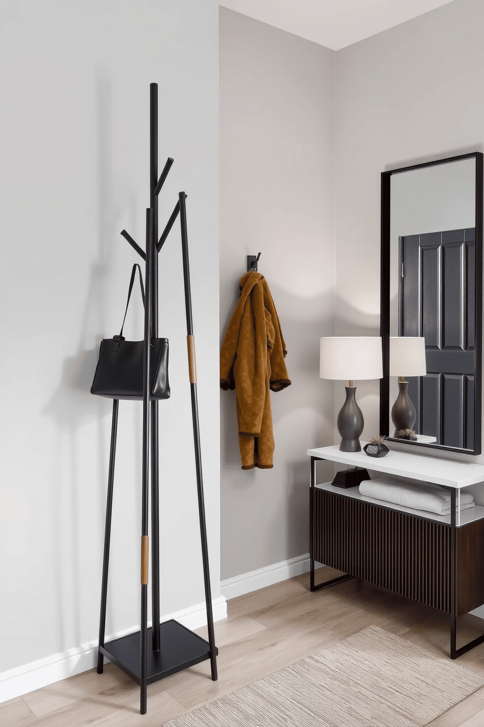 A chic coat stand for an entryway features a sleek, modern design made of matte black metal with elegant wooden accents. It stands against a light gray wall, providing a stylish yet functional space for hanging coats and bags. Narrow foyer design ideas incorporate a minimalist console table with a unique geometric shape, topped with decorative items like a small plant and a stylish lamp. The walls are adorned with a large mirror to enhance light and create the illusion of space, while a runner rug adds warmth and texture underfoot.