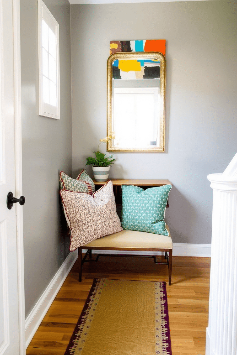 A cozy foyer featuring a narrow console table against the wall, adorned with colorful accent pillows in various patterns and textures. The walls are painted in a soft gray, and a statement mirror hangs above the table, reflecting natural light from a nearby window. The floor is lined with a stylish runner that adds warmth and visual interest, while a small potted plant sits on the console for a touch of greenery. Above the table, a piece of abstract art in vibrant colors complements the pillows, creating an inviting and cheerful entryway.