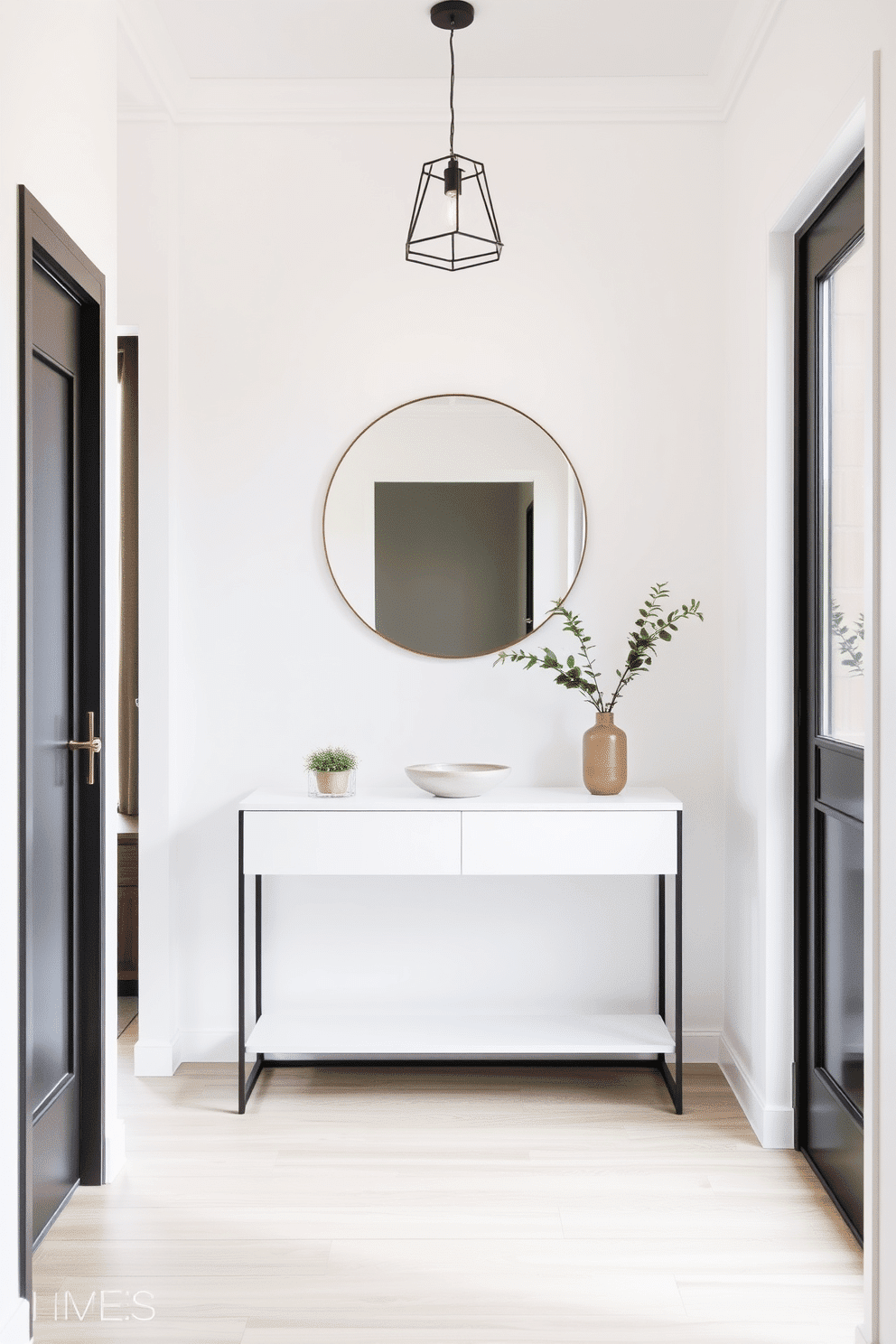 A narrow foyer features a sleek console table with a minimalist design, topped with a simple decorative bowl and a small potted plant. The walls are painted in a soft white hue, and a large round mirror hangs above the table, reflecting natural light from a nearby window. The floor is adorned with light-colored wood planks, enhancing the airy feel of the space. A single pendant light with a geometric design hangs from the ceiling, adding a modern touch while maintaining the clean aesthetic.