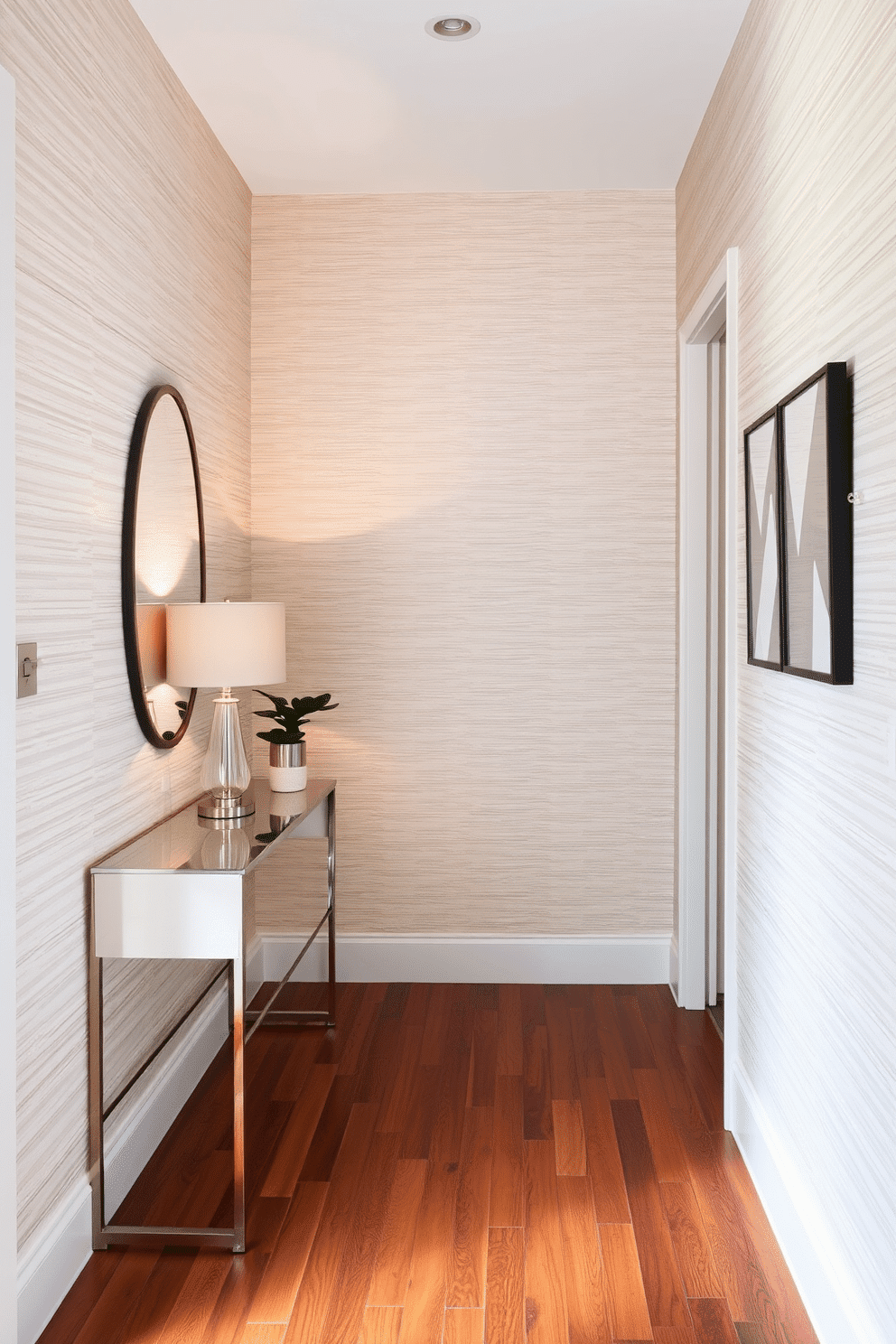 A narrow foyer adorned with textured wallpaper creates an inviting atmosphere. The wallpaper features a subtle geometric pattern in soft hues, enhancing the sense of depth and sophistication. To one side, a sleek console table with a minimalist design showcases a statement lamp and a small potted plant. The flooring is a rich hardwood, contrasting beautifully with the wallpaper and adding warmth to the space.