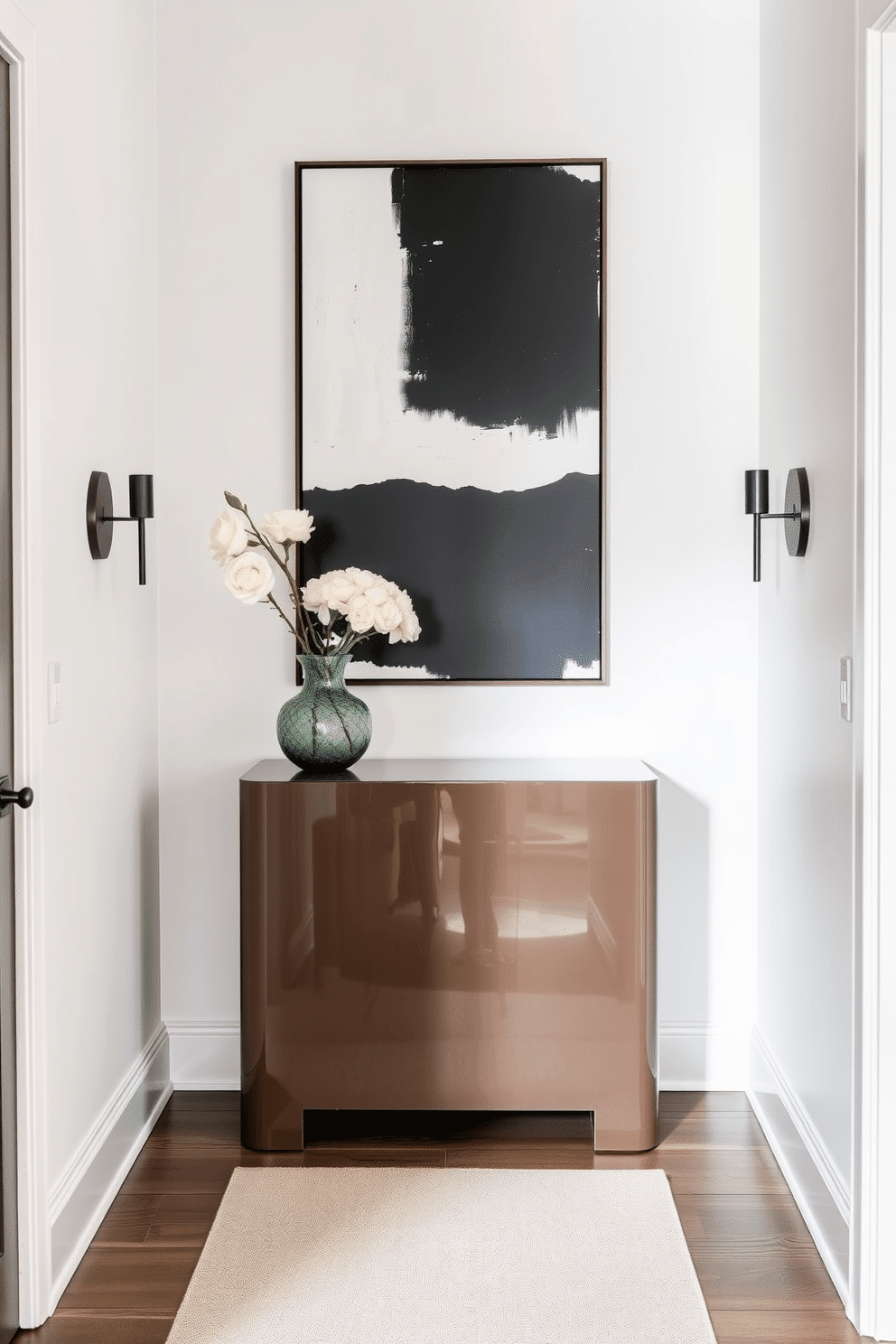 A narrow foyer featuring a sleek console table with a glossy finish, topped with a statement oversized artwork that draws the eye. The walls are painted in a soft, neutral hue, complemented by a stylish runner rug that adds warmth and texture to the space. Incorporate a tall, narrow mirror above the console table to enhance the sense of depth and light. Flanking the entryway, a pair of elegant sconces provide soft illumination, creating an inviting atmosphere as guests enter.