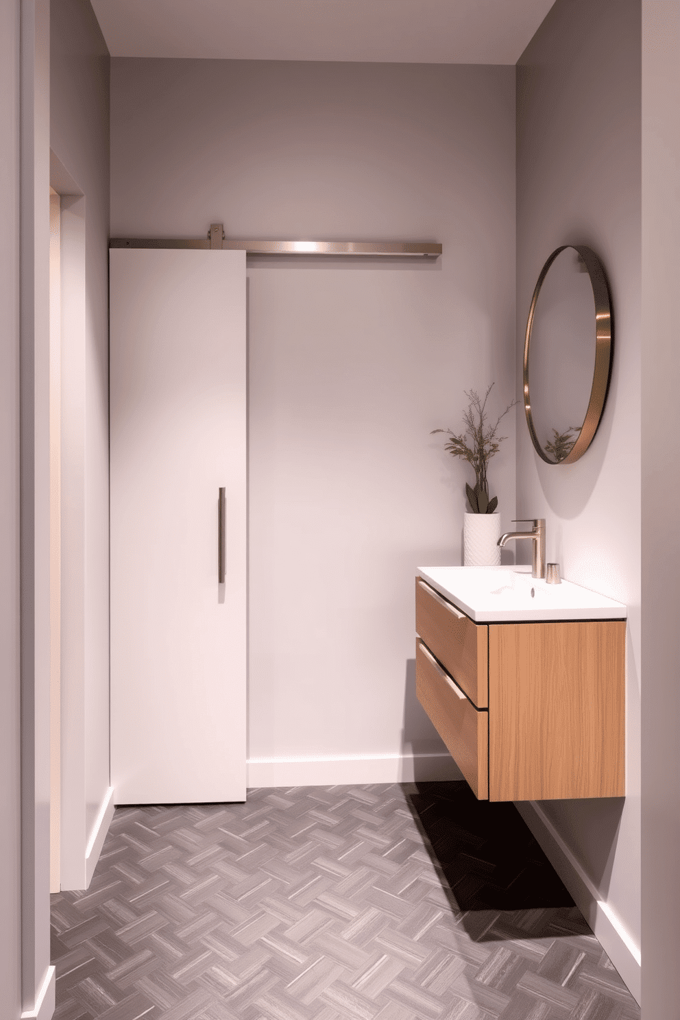 A narrow powder room features a sleek sliding door that elegantly opens into the space, maximizing the available floor area. The walls are adorned with a soft, light gray paint, and the floor is covered in a stylish, dark herringbone tile that adds depth and sophistication. A compact floating vanity with a polished white countertop is positioned against one wall, complemented by a round mirror with a minimalist frame. Decorative accents, such as a small potted plant and a chic hand towel, enhance the room's inviting atmosphere while maintaining a clean and modern aesthetic.