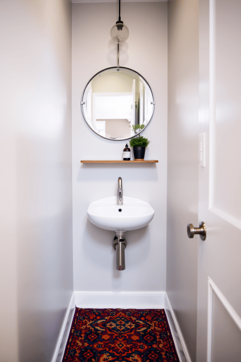 A narrow powder room featuring a sleek, wall-mounted sink with a modern faucet. The walls are painted a soft, light gray, complemented by a vibrant, patterned rug that adds warmth and character to the space. Above the sink, a stylish round mirror with a decorative frame reflects the ambient light. A small shelf holds decorative items, while a potted plant in the corner brings a touch of greenery to the compact area.