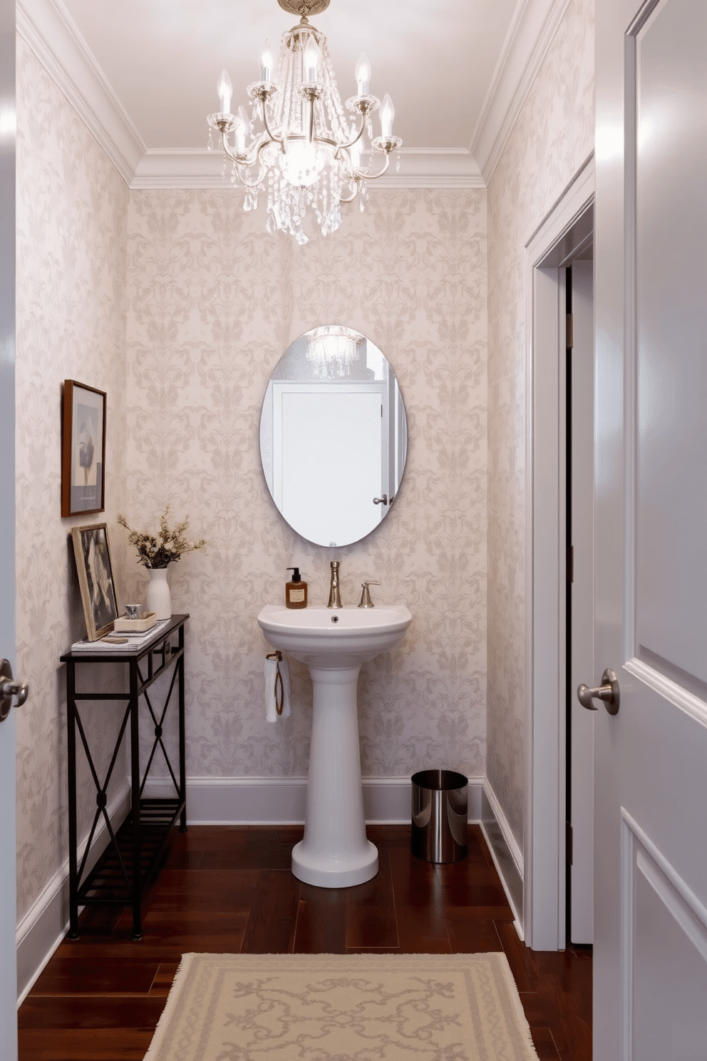 A narrow powder room features a stunning small chandelier that adds a touch of elegance to the space. The walls are adorned with a soft, light gray wallpaper, while a sleek pedestal sink complements the chic design. To maximize functionality, a narrow console table is placed against one wall, topped with decorative items and a small mirror. The flooring consists of dark hardwood, creating a warm contrast with the lighter elements in the room.