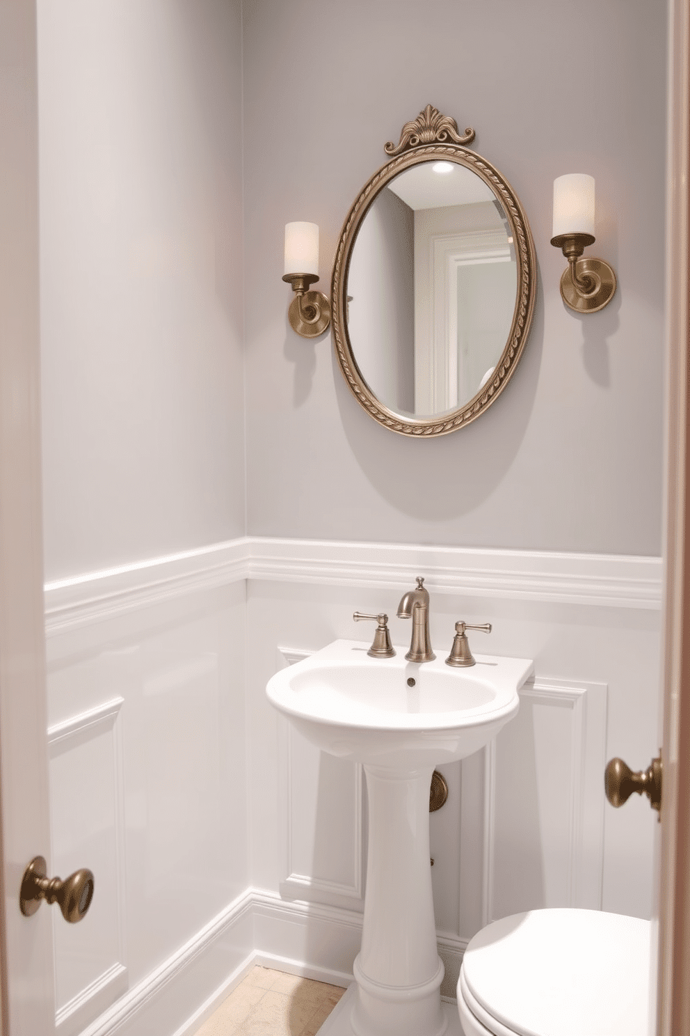 A narrow powder room features a half-wall that separates the toilet area from the sink space, enhancing privacy while maintaining an open feel. The walls are adorned with a soft, light gray paint, complemented by elegant wainscoting in a crisp white. The sink is a sleek pedestal style, paired with a vintage-inspired faucet in brushed nickel. Above the sink, a round mirror with a decorative frame reflects stylish wall sconces that provide warm, ambient lighting.