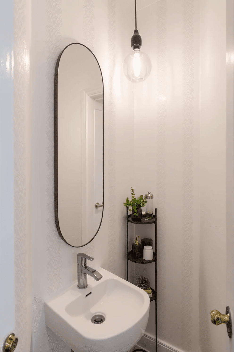 A narrow powder room featuring light-colored walls that enhance the sense of space and airiness. The design includes a sleek, wall-mounted sink with a minimalist faucet, complemented by a tall, narrow mirror that reflects light throughout the room. Soft, neutral tones dominate the decor, with a delicate wallpaper pattern adding subtle texture. A small, stylish shelving unit displays decorative items and fresh greenery, while a chic pendant light fixture provides warm illumination.