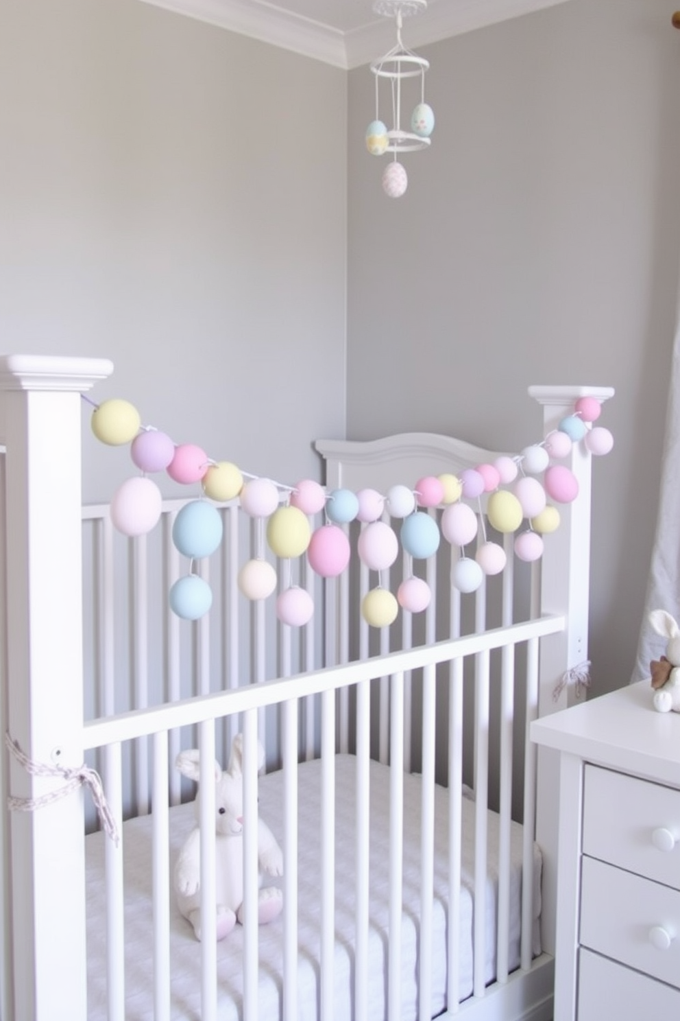 A cozy nursery adorned for Easter. A pastel-colored egg garland is draped across the white crib railing, adding a festive touch to the room. The soft hues of pink, blue, and yellow in the garland complement the light gray walls and the white furniture. A plush bunny sits in the corner of the crib, while a delicate mobile with Easter-themed ornaments hangs above.