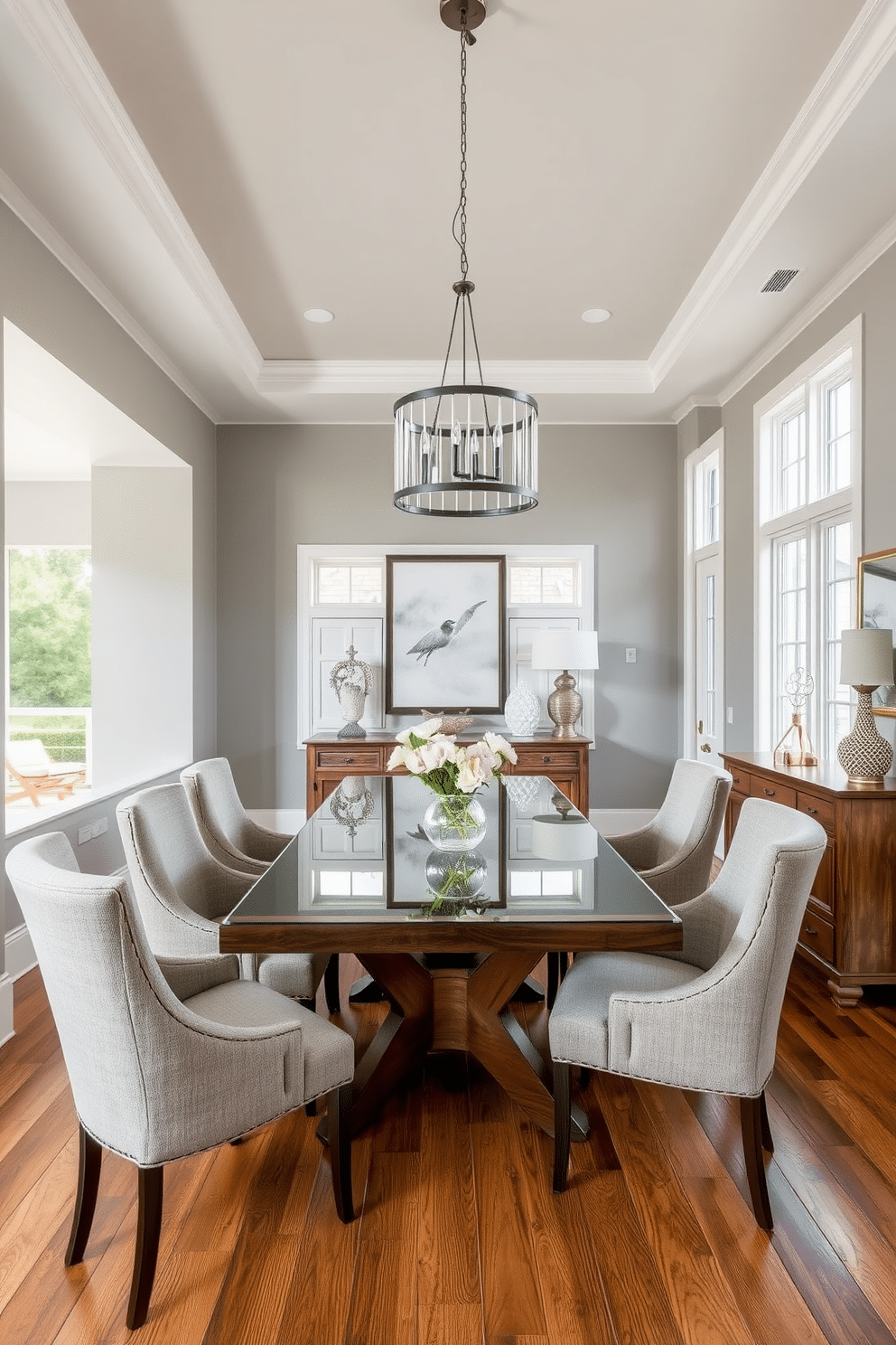 A transitional dining room that seamlessly blends modern and traditional elements. The space features a large wooden dining table with a sleek glass top, surrounded by upholstered chairs in a neutral fabric. Above the table, a contemporary chandelier adds a touch of elegance, while a vintage sideboard against the wall showcases decorative tableware. The walls are painted in a soft gray, and large windows allow natural light to flood the room, highlighting the warm wood tones of the flooring.