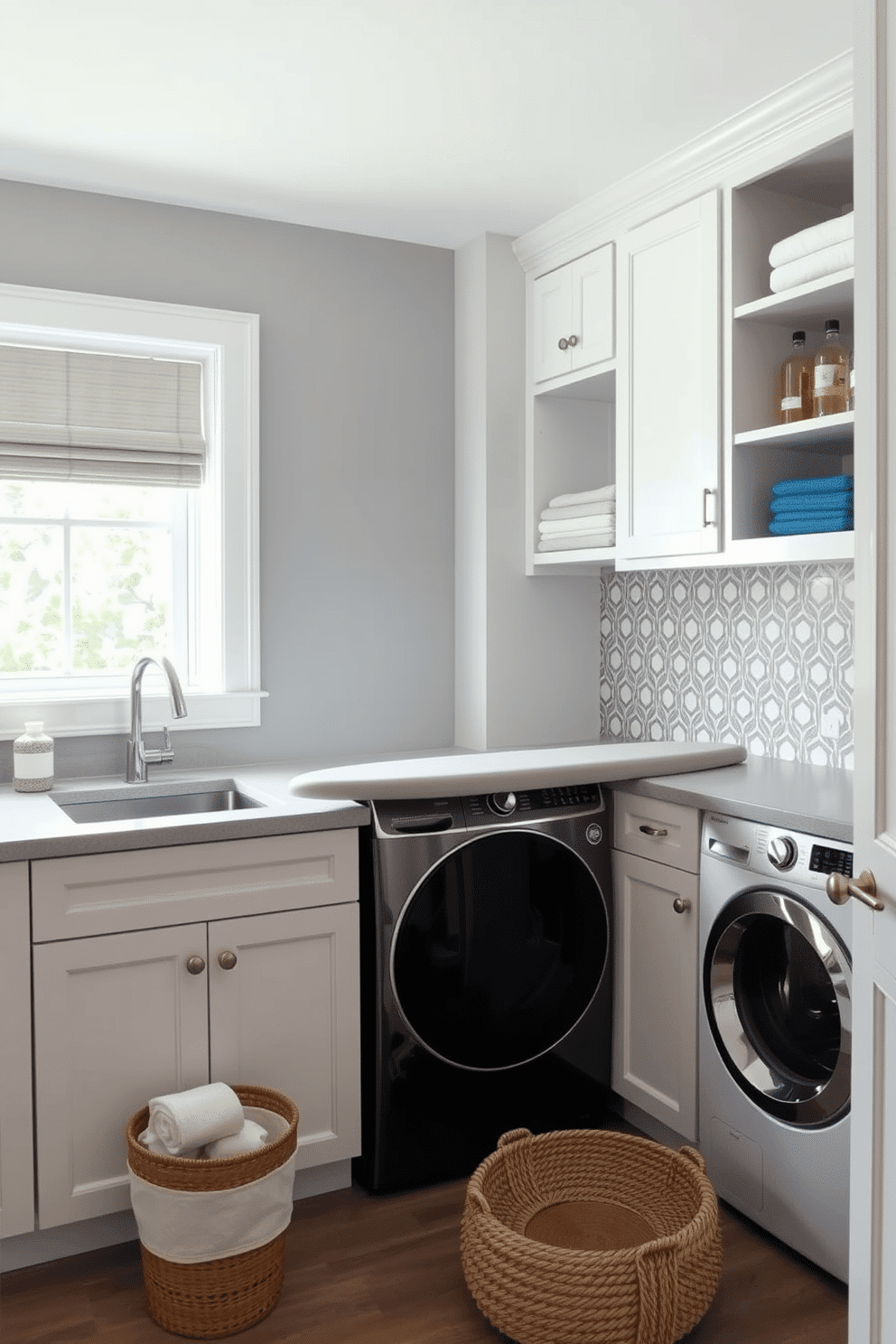 A stylish laundry room featuring a built-in ironing board seamlessly integrated into the cabinetry. The space is illuminated by natural light filtering through a window, with soft gray walls and white cabinetry providing a clean, modern aesthetic. The laundry area includes a spacious countertop for folding clothes, complemented by open shelving above for easy access to laundry supplies. A chic backsplash in a geometric pattern adds a touch of personality, while a woven basket sits on the floor for storing linens.