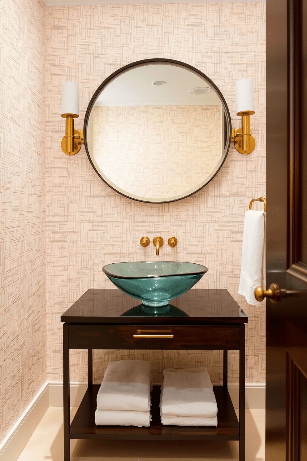 A striking powder room features a unique vessel sink crafted from hand-blown glass, positioned atop a sleek, dark wood vanity. The walls are adorned with a textured wallpaper in soft pastels, complemented by elegant brass fixtures and a large, round mirror that reflects the room's ambiance.