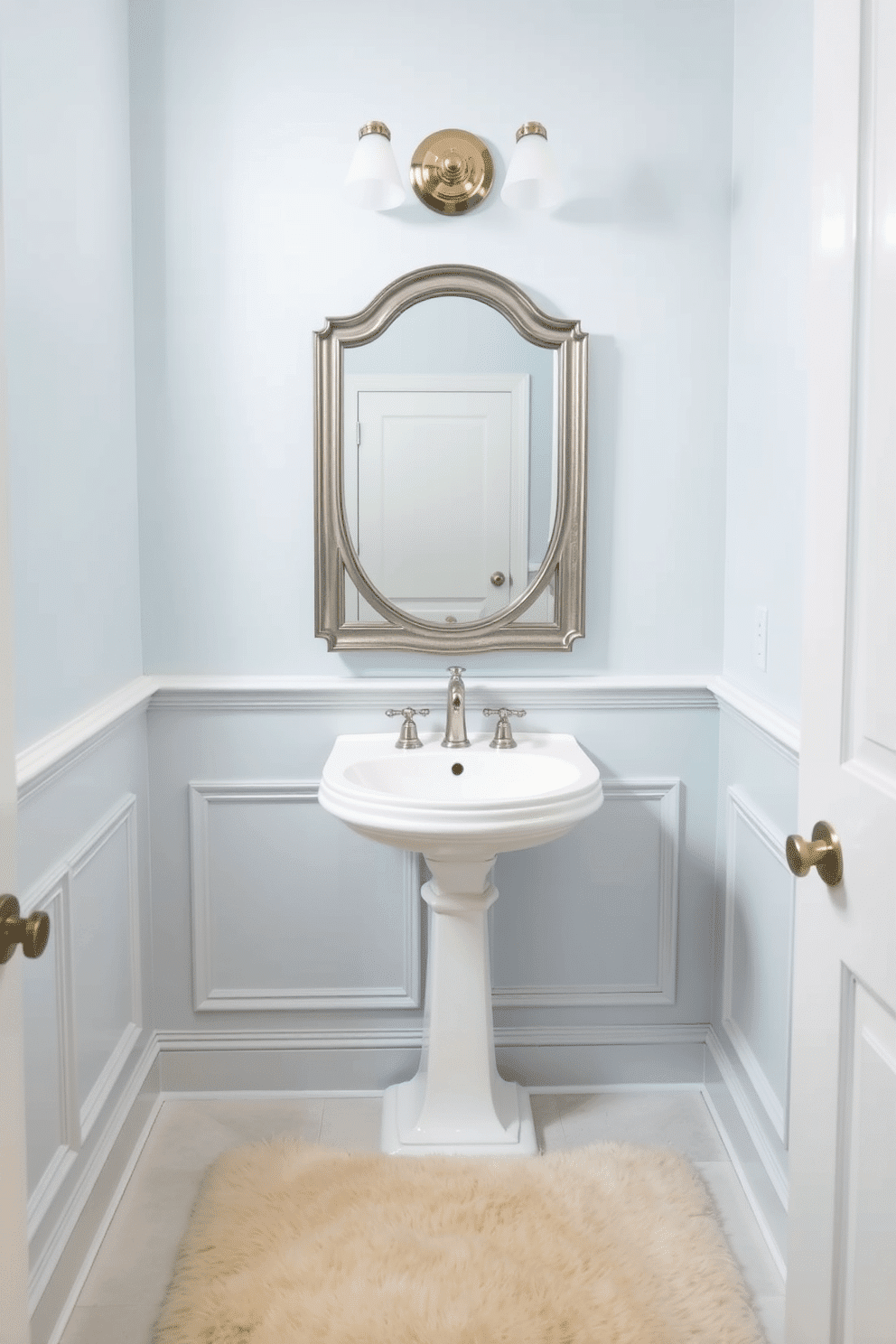 A soft pale blue hue envelops the powder room, creating a serene and calming atmosphere. The walls are adorned with delicate wainscoting, enhancing the elegance of the space while providing a subtle contrast to the soothing color. A sleek white pedestal sink is complemented by a vintage-style mirror framed in brushed silver. To add warmth, a plush cream rug lies beneath, while soft lighting fixtures with a brushed nickel finish illuminate the room, casting a gentle glow.