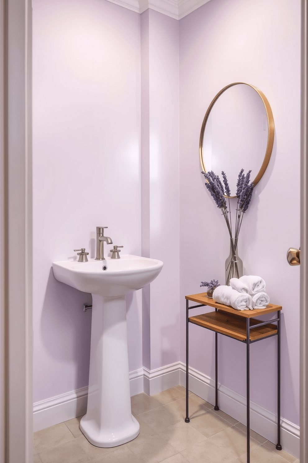 A serene powder room featuring walls painted in a soft pale lilac, creating a delicate and inviting atmosphere. The space is accented with a sleek white pedestal sink and a round mirror framed in brushed gold, enhancing the room's elegance. The floor is adorned with light gray tiles that complement the lilac walls, adding a touch of sophistication. A small wooden shelf holds neatly rolled white towels and a decorative vase with fresh lavender, completing the tranquil aesthetic.