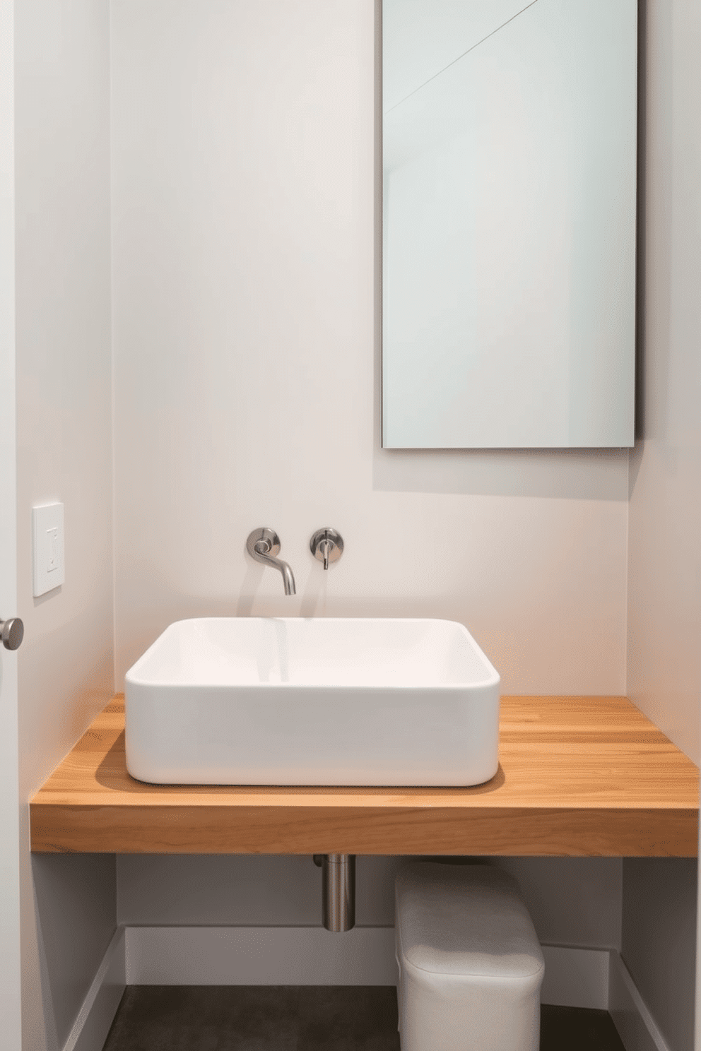 A stylish trough sink with a minimalistic design takes center stage in this elegant powder room. The sink is crafted from smooth white ceramic, complemented by a sleek, wall-mounted faucet in brushed nickel. Surrounding the sink, a floating vanity made of natural wood adds warmth to the space. The walls are adorned with soft gray paint, and a large frameless mirror reflects the light, enhancing the room's airy feel.