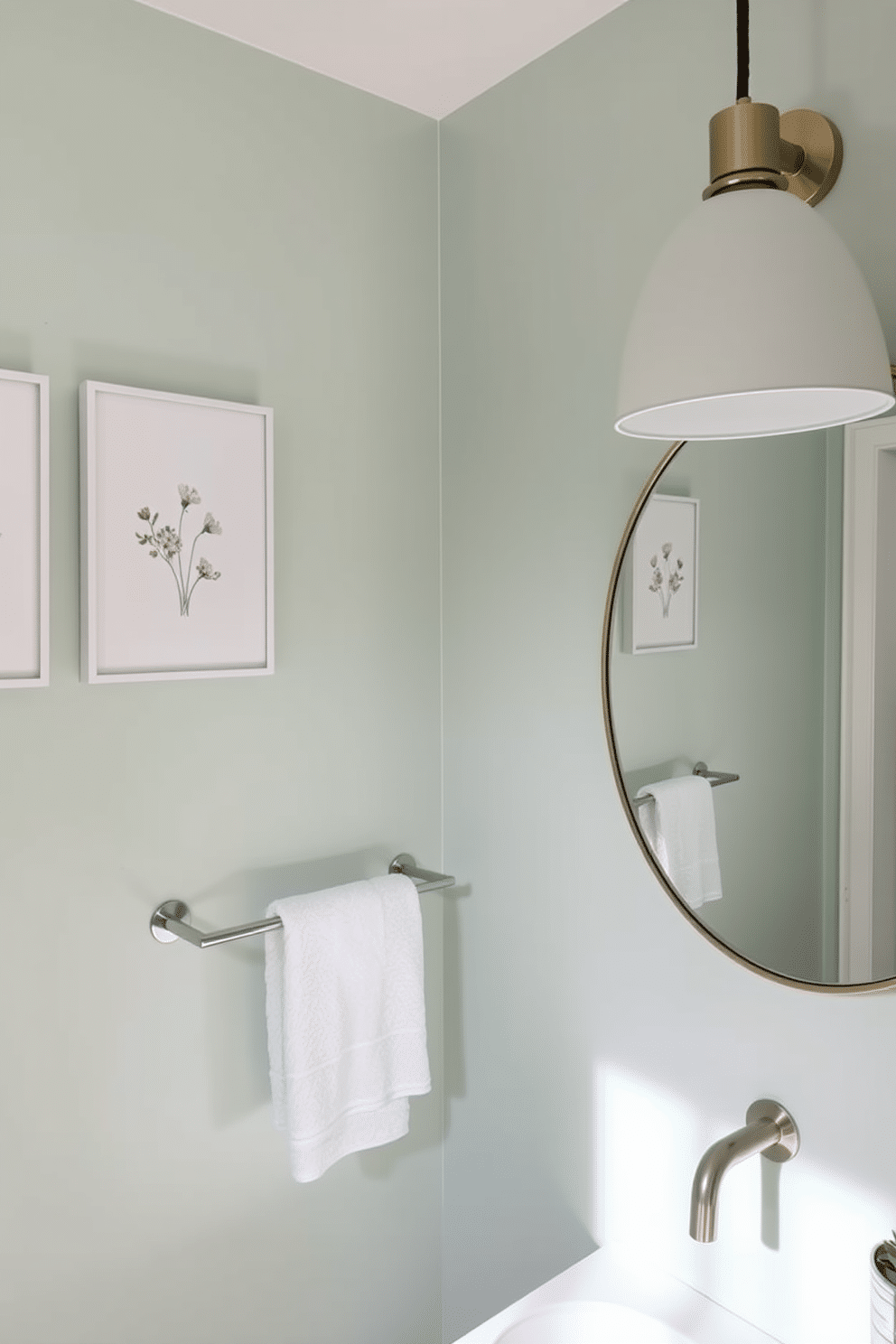 A serene powder room featuring soft pastel colors, with walls painted in a gentle mint green. The decor includes delicate floral wall art and a chic, minimalist floating shelf adorned with small potted plants. The space is complemented by a stylish round mirror with a soft gold frame, reflecting the light from a modern pendant lamp. A plush white towel hangs elegantly on a sleek towel rack, enhancing the calming ambiance.