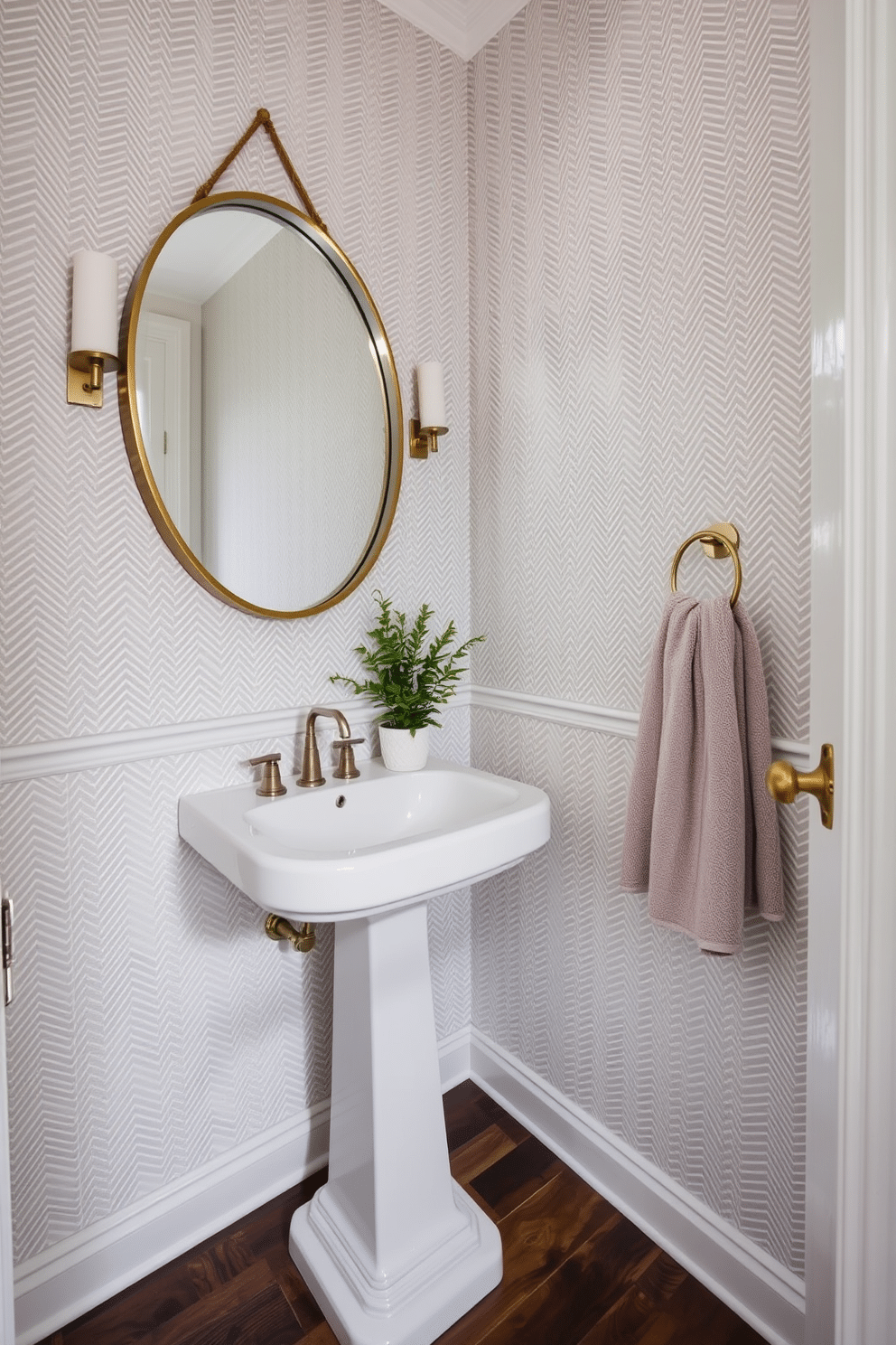 A chic powder room adorned with a herringbone-patterned wallpaper in soft gray tones, creating a sophisticated and inviting atmosphere. The room features a sleek white pedestal sink with a polished chrome faucet and a round mirror framed in brushed brass, reflecting the elegant design. The floor is laid with dark hardwood, contrasting beautifully with the light wallpaper and enhancing the room's warmth. A small potted plant sits on the sink, adding a touch of greenery, while a plush hand towel in a complementary shade hangs neatly nearby.