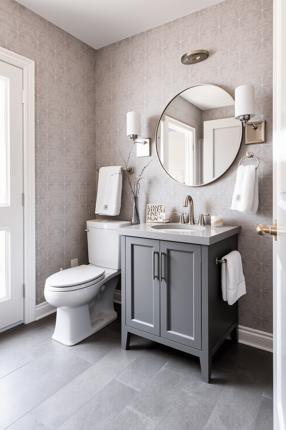 A chic powder room featuring a monochromatic color scheme, with soft gray wallpaper adorned with subtle geometric patterns. The sleek vanity, finished in a matching gray tone, is complemented by a minimalist round mirror and elegant brushed nickel fixtures. The floor is covered with large, matte gray tiles that enhance the room's spacious feel. Accents of white, such as fluffy towels and decorative accessories, add a touch of contrast, creating a sophisticated and cohesive look.